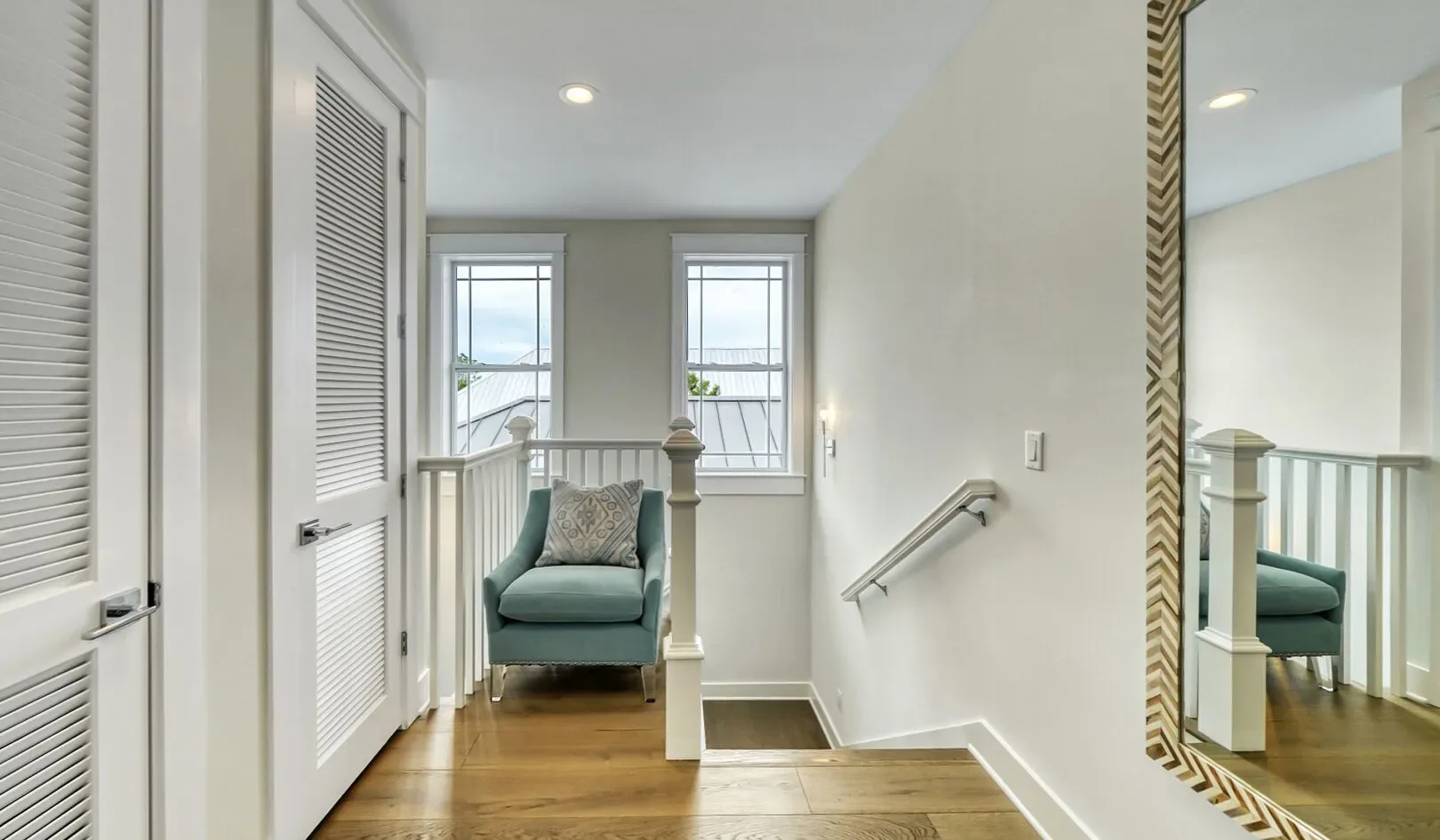 A small landing with a green upholstered seat, two windows, and stairs.