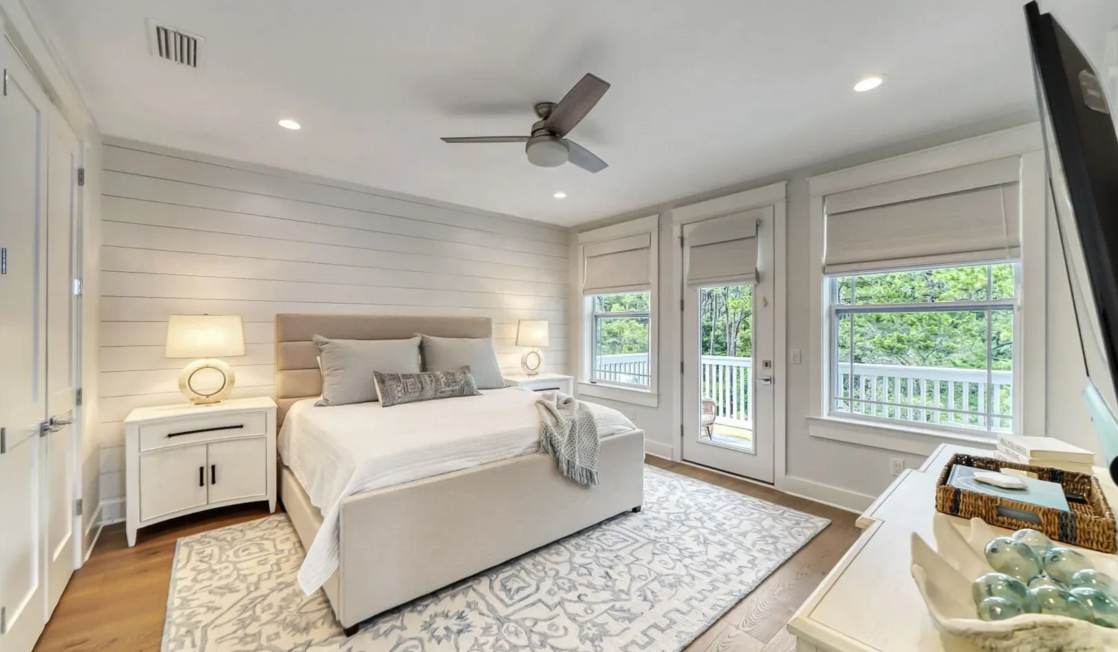 A bright bedroom with a neatly made bed and windows overlooking greenery.