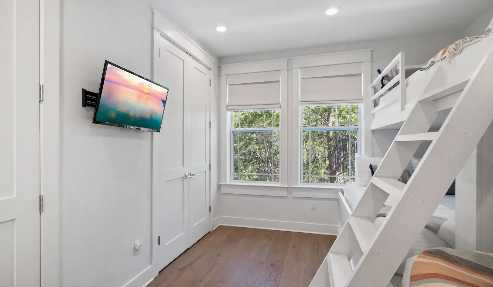 A bright bedroom with a wall-mounted television, windows, and a bunk bed.
