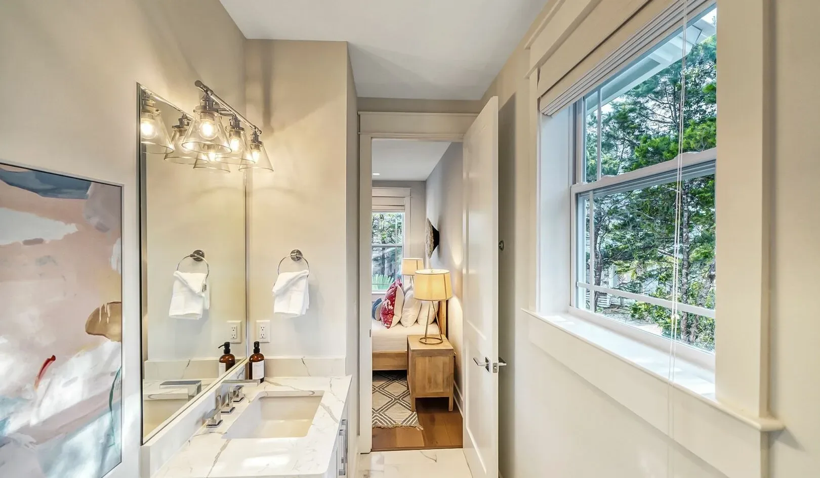 A bright bathroom with a sink, mirror, and large window.