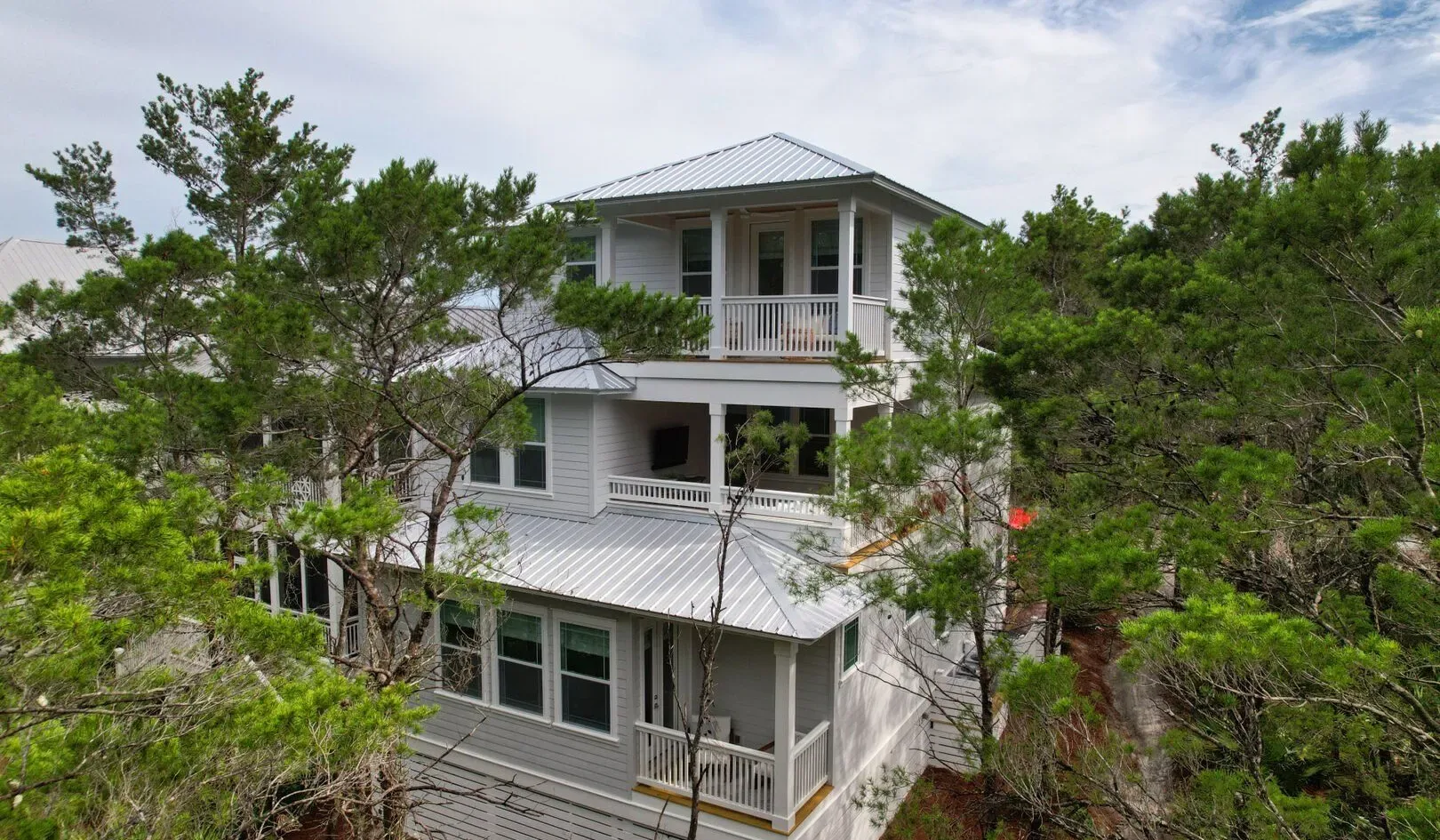 A multi-level house with white exterior walls and balconies stands among trees.