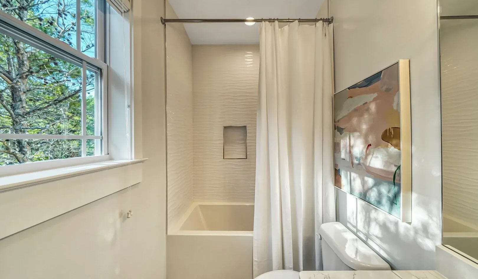 A bright bathroom with a bathtub, shower curtain, and large window.
