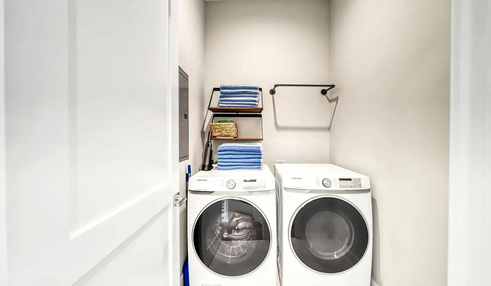 A laundry area with a front-loading washer and dryer beneath shelves of folded towels.