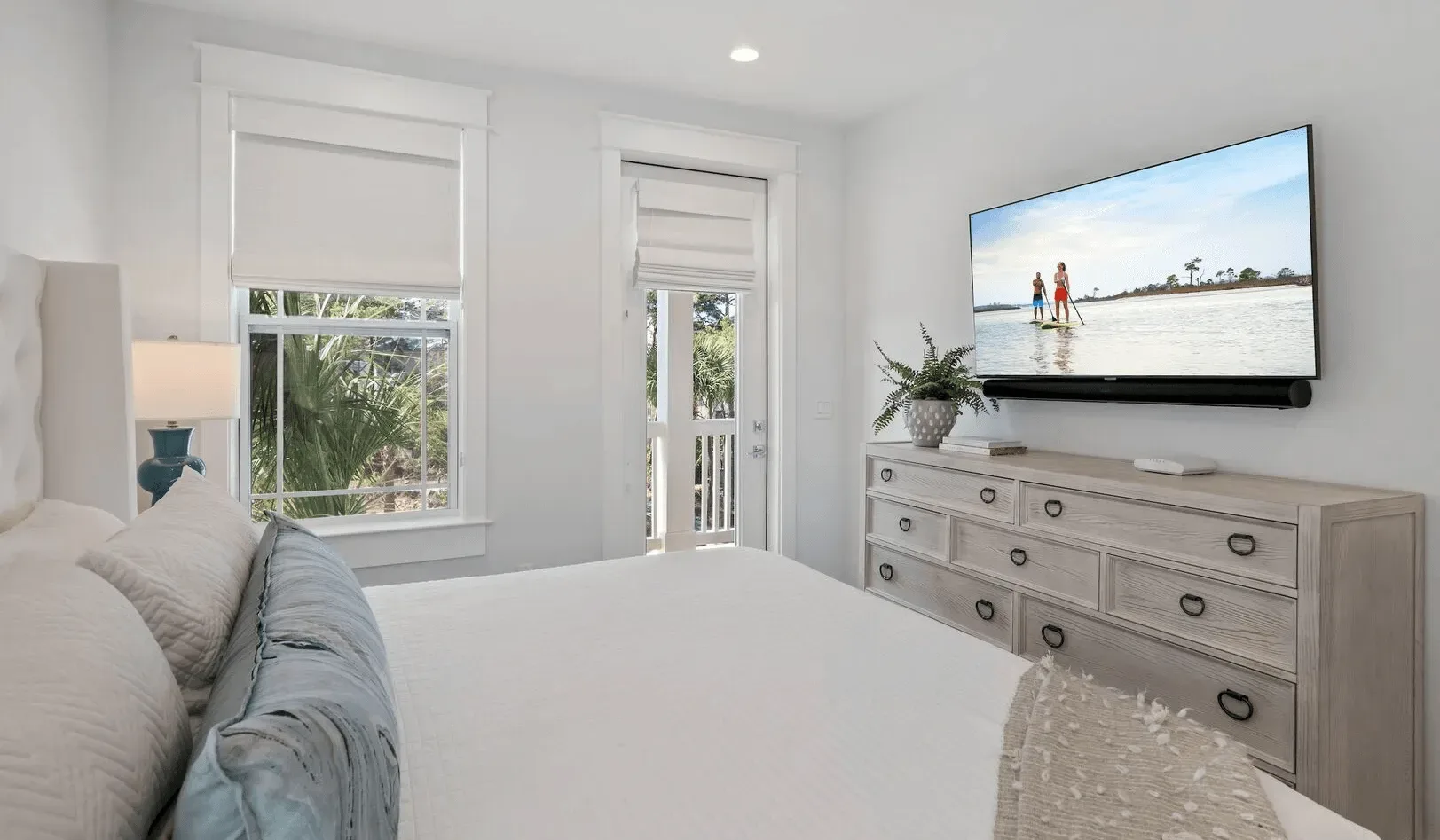 A bright bedroom with a bed, windows, and a television on a dresser.