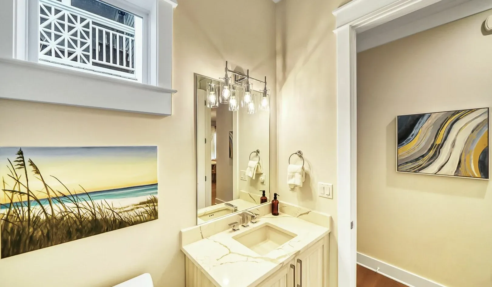 A bright bathroom vanity sits beneath a large mirror, with artwork on the walls.