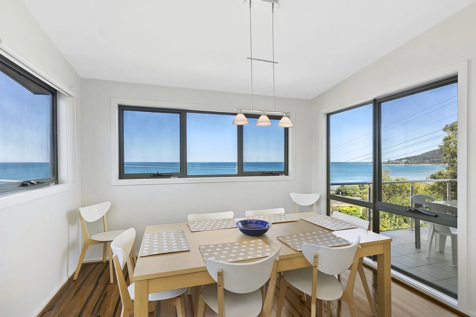 Comedor con una mesa de madera y vistas al mar a través de grandes ventanales.