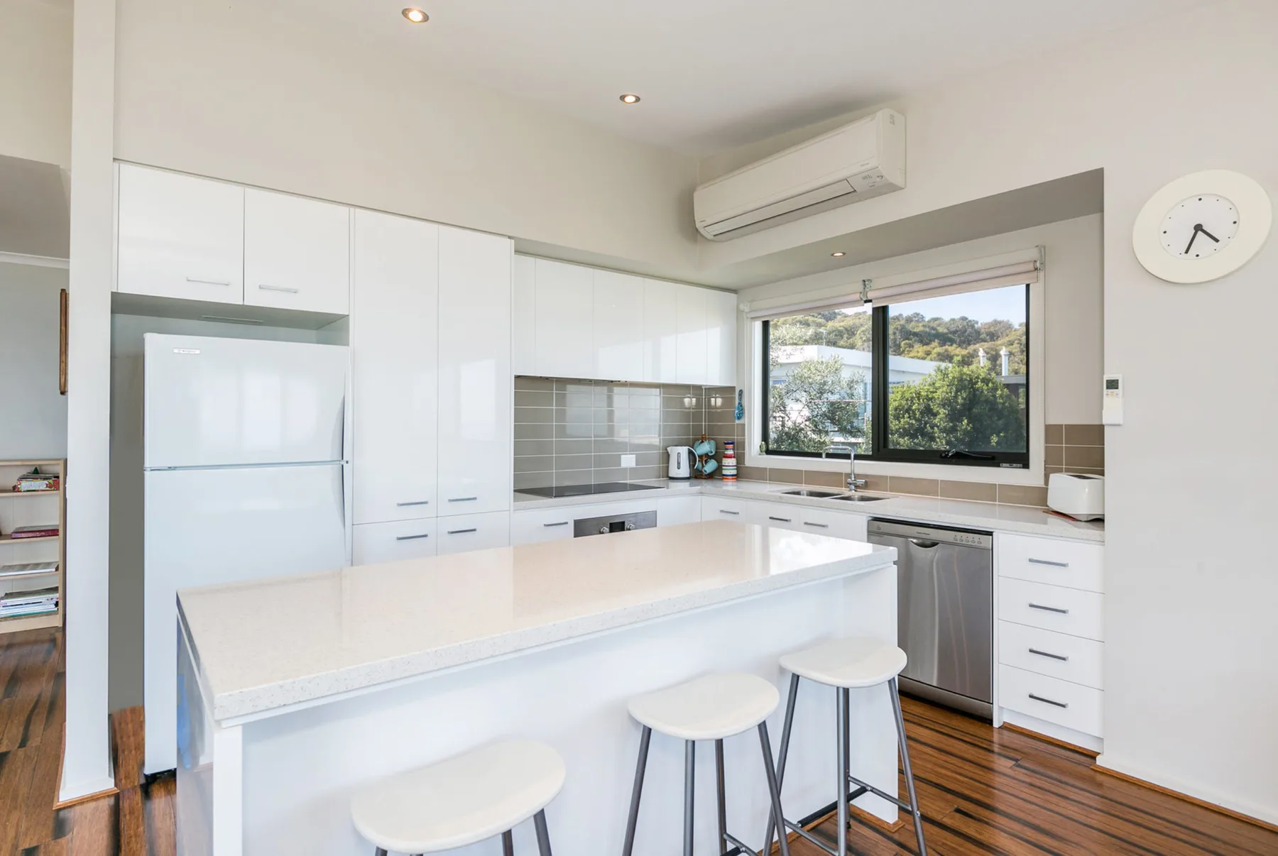 Una cocina luminosa con isla central, taburetes y una ventana con vistas a la vegetación.