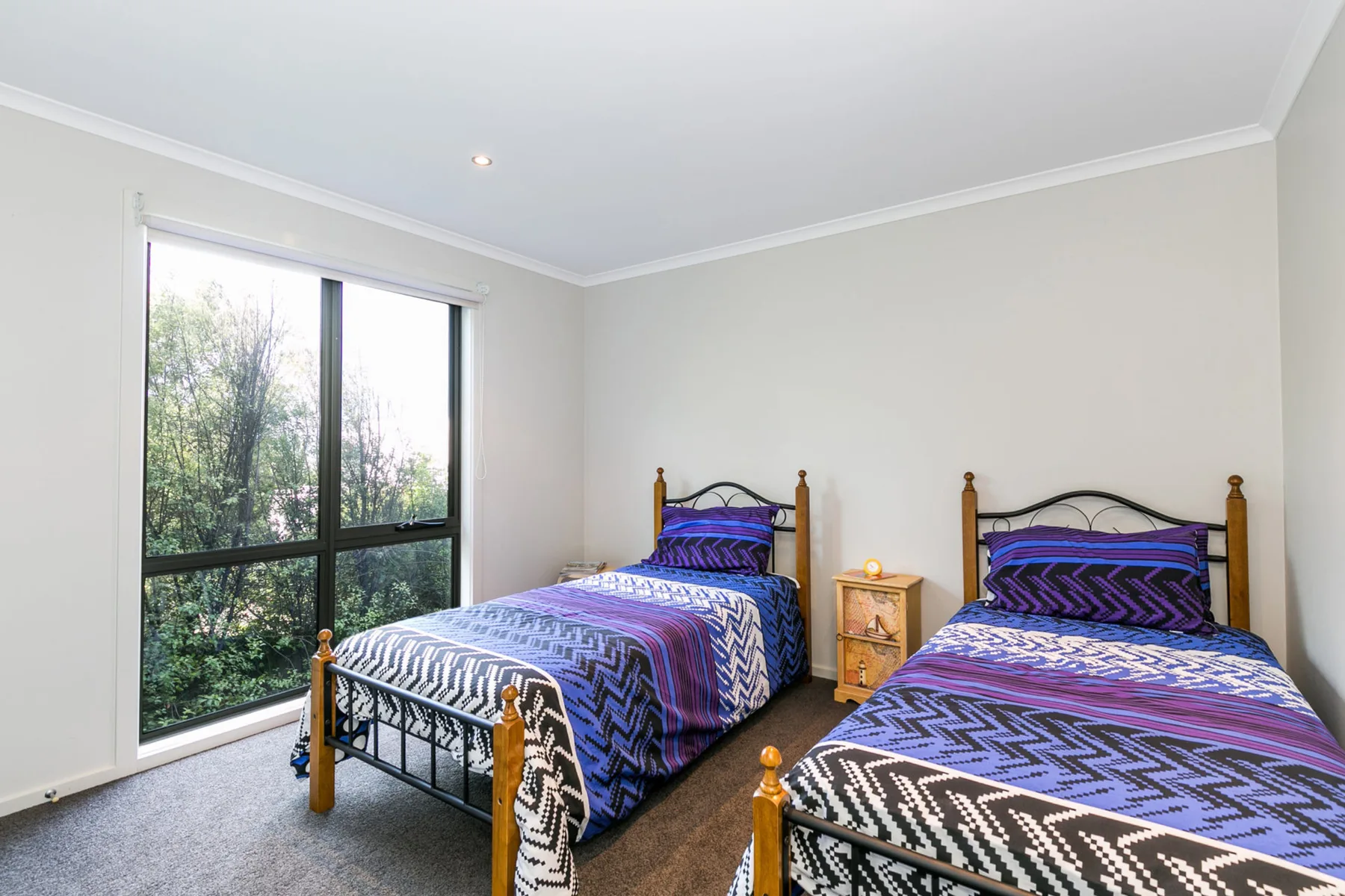 Dormitorio con dos camas, ropa de cama estampada y una ventana amplia con vistas a la vegetación.