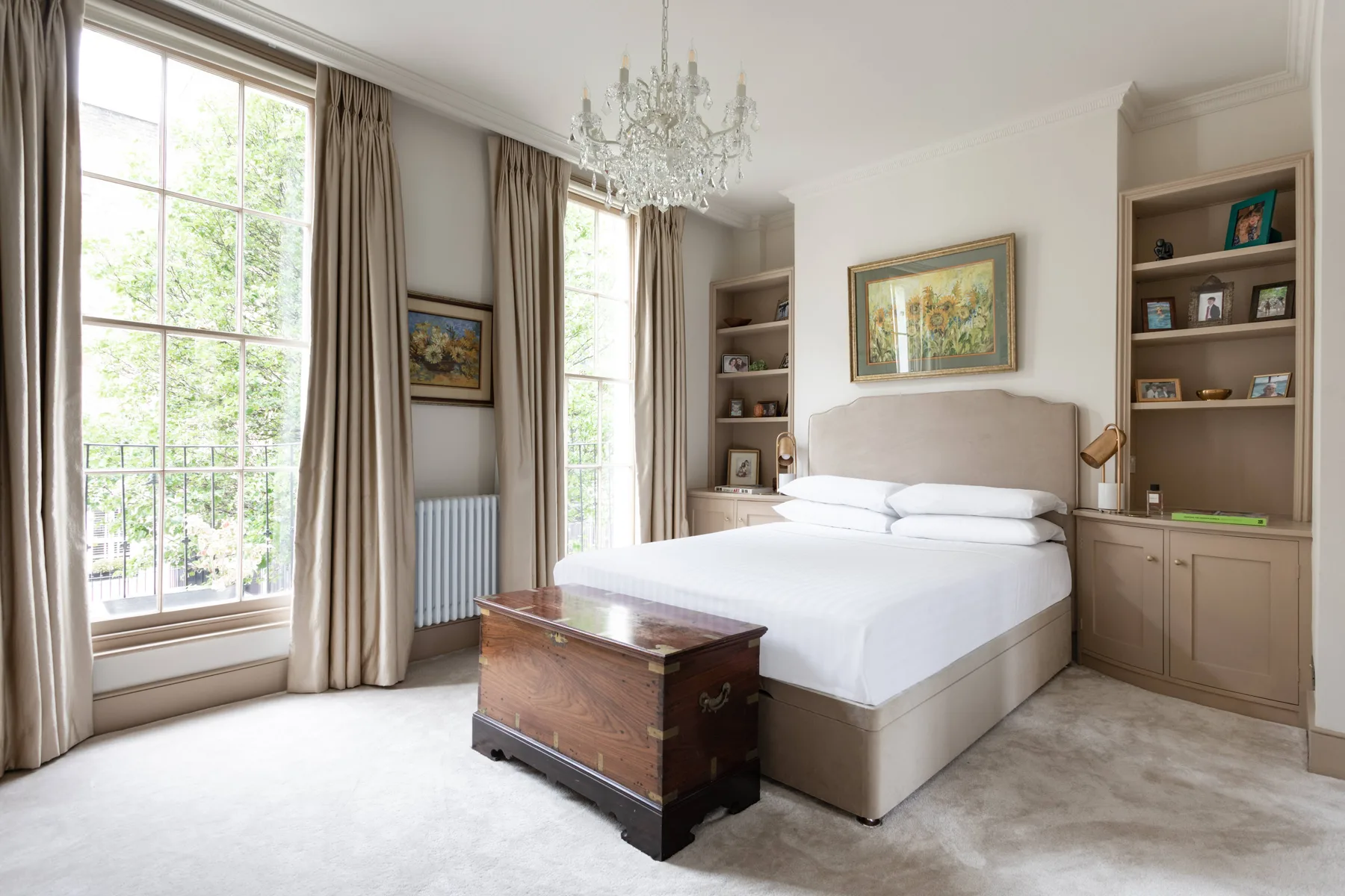 A bright bedroom with a large bed, tall windows, and built-in shelving.