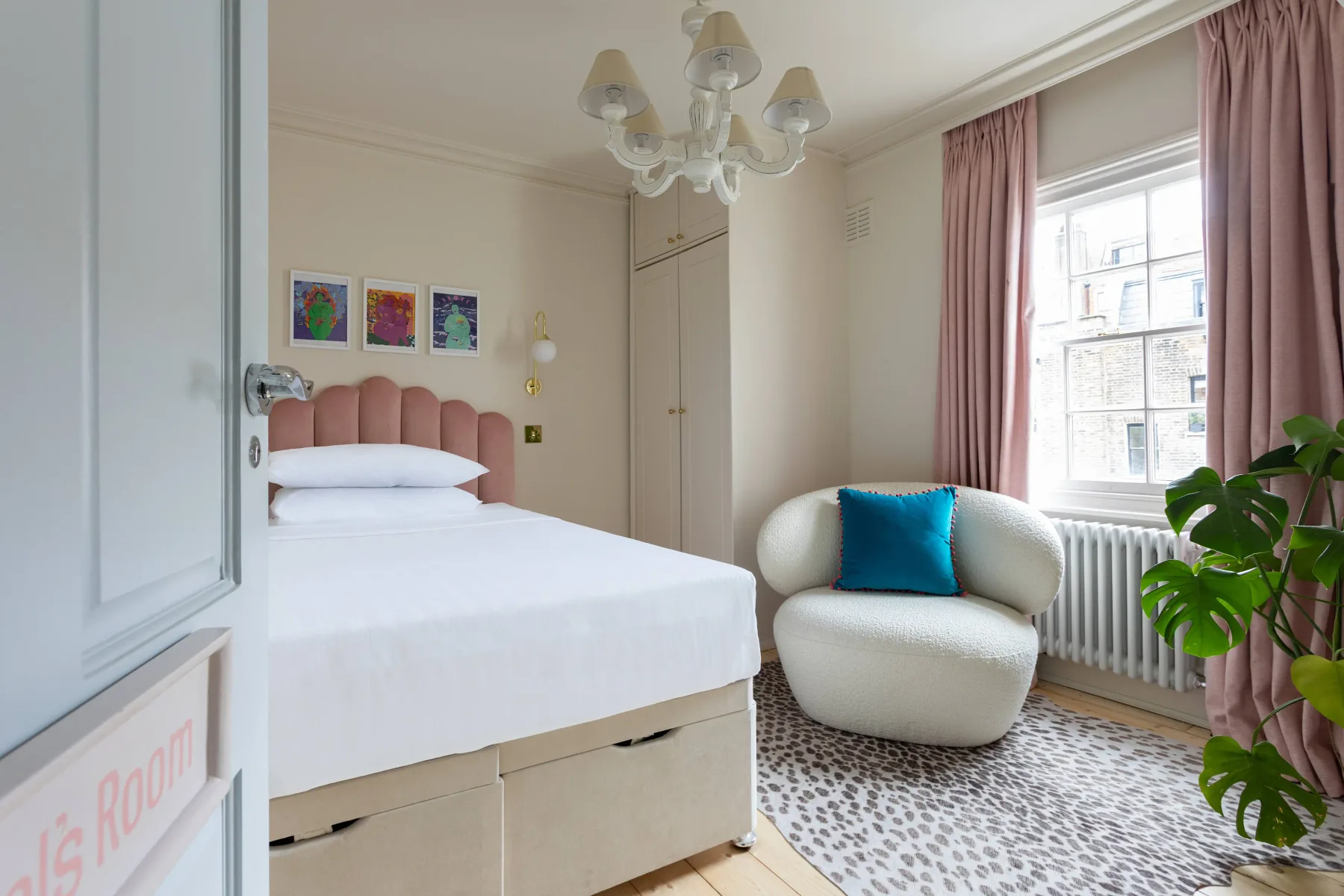 A bedroom with a neatly made bed, a rounded chair, and a large window.