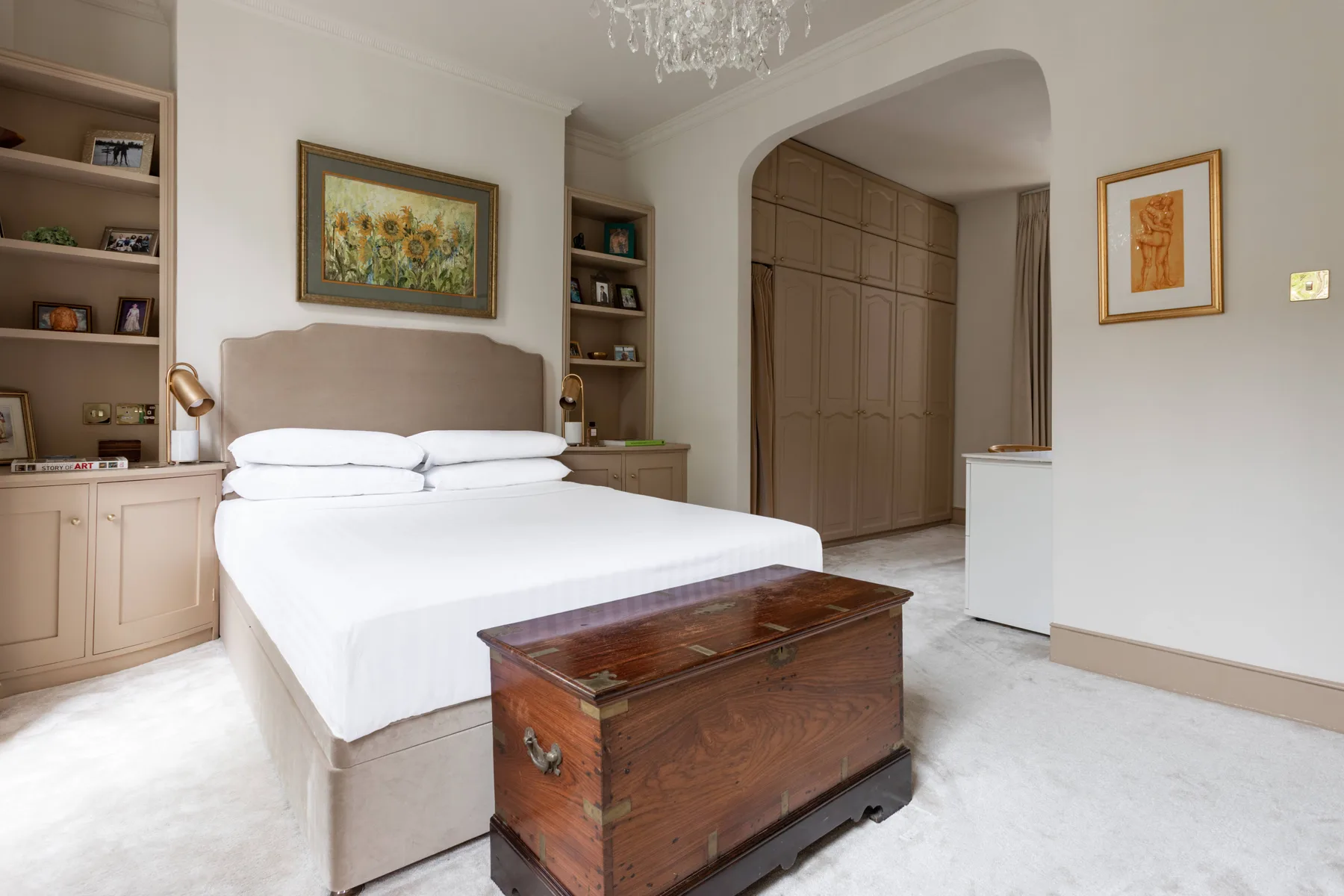 A bedroom with a neatly made bed and a wooden chest at its foot.