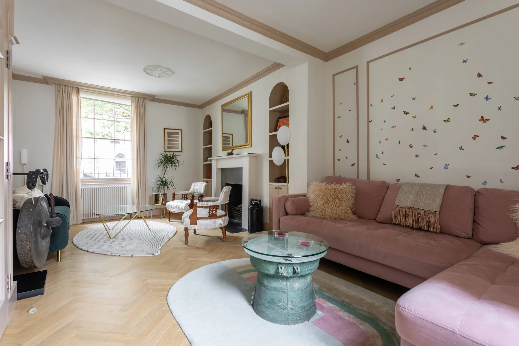 A living room with pink seating, a round glass table, and a fireplace.