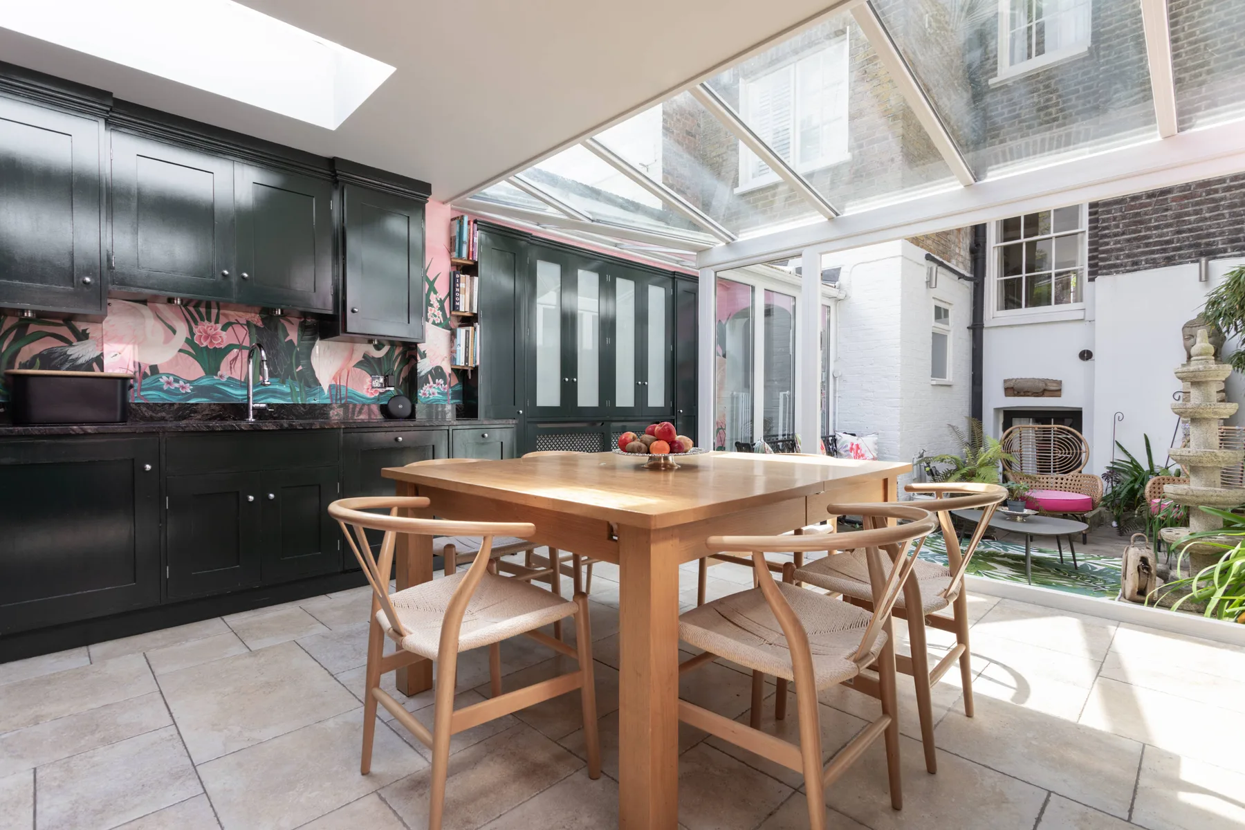 A dining area with a wooden table and chairs beneath a glass roof.