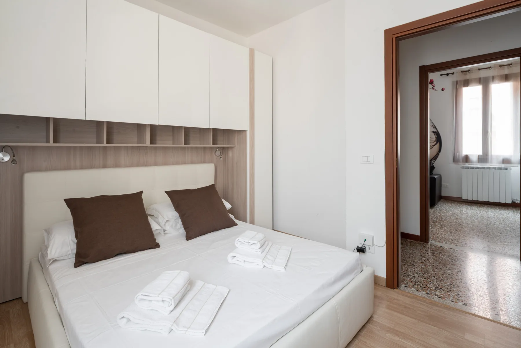 Un dormitorio con una cama blanca, almohadas marrones y armarios empotrados.