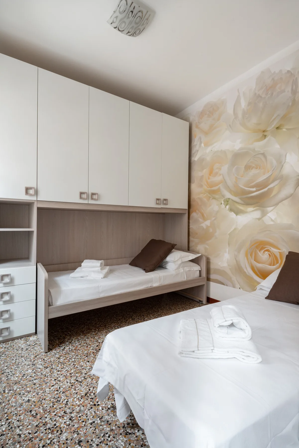 Un dormitorio con dos camas, armarios empotrados y decoración floral en la pared.