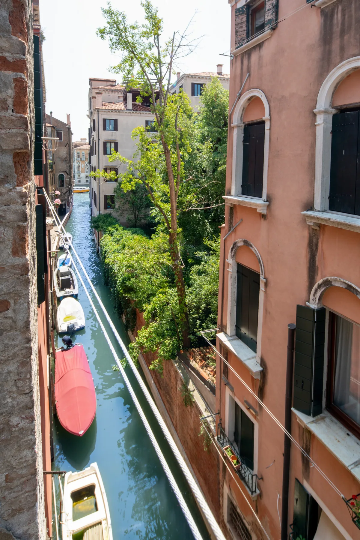 Un canal estrecho pasa entre edificios, con barcas y árboles frondosos junto al agua.