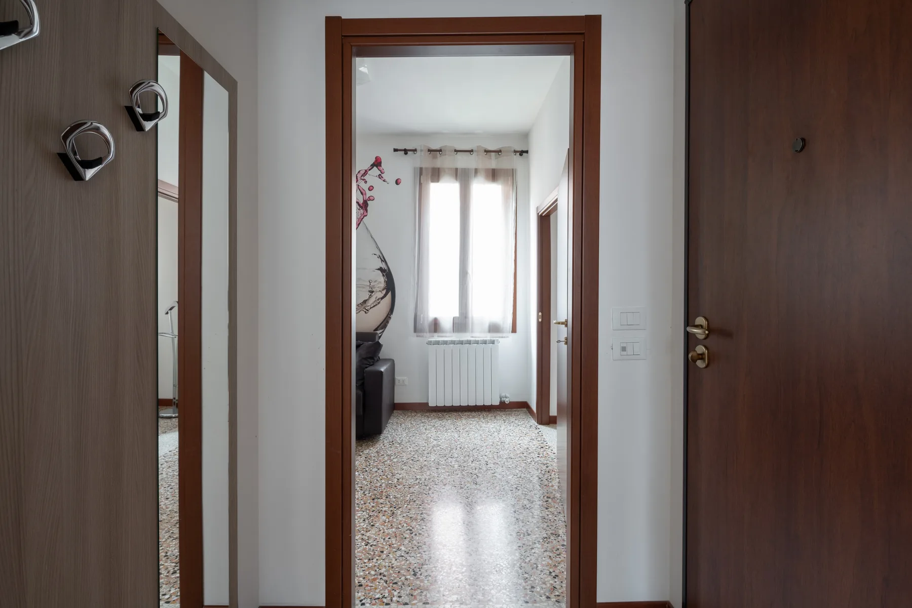 Una puerta da a una habitación luminosa con una ventana y un radiador.