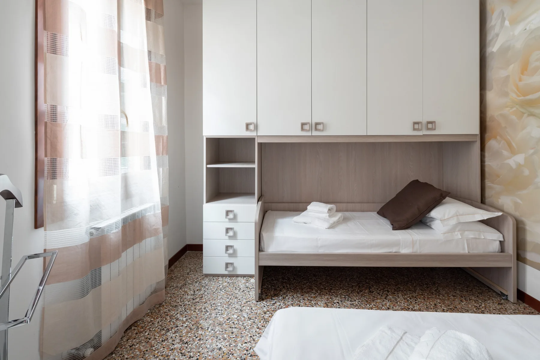 Un dormitorio con una cama empotrada y ropa de cama blanca junto a una ventana con cortinas.