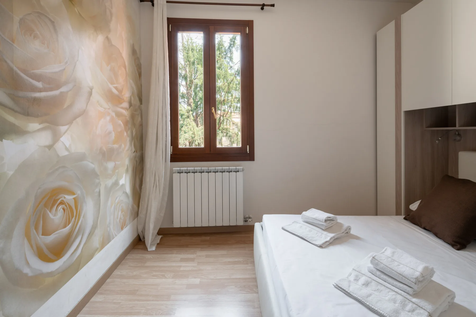 Un dormitorio con una cama junto a una ventana y un mural floral.