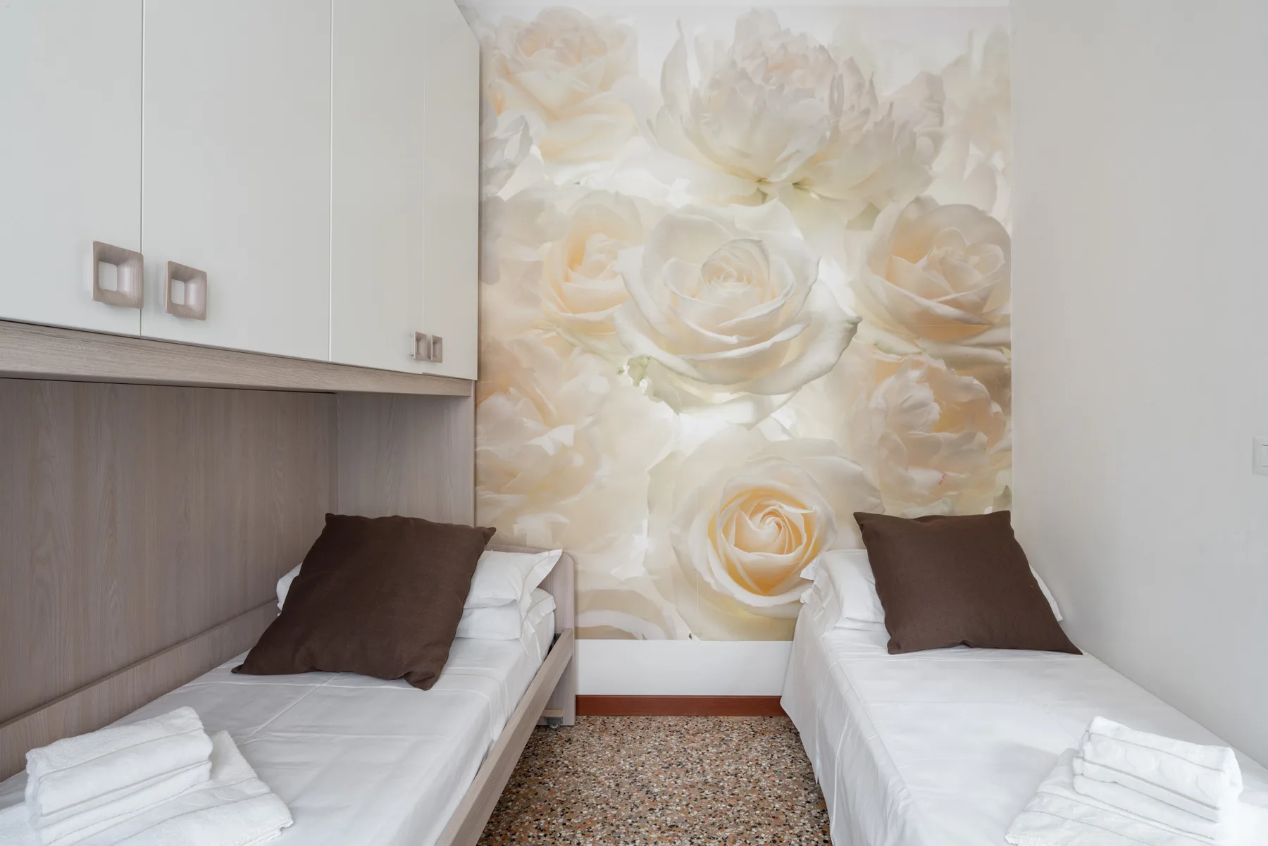 Un dormitorio con dos camas y un mural floral en la pared.
