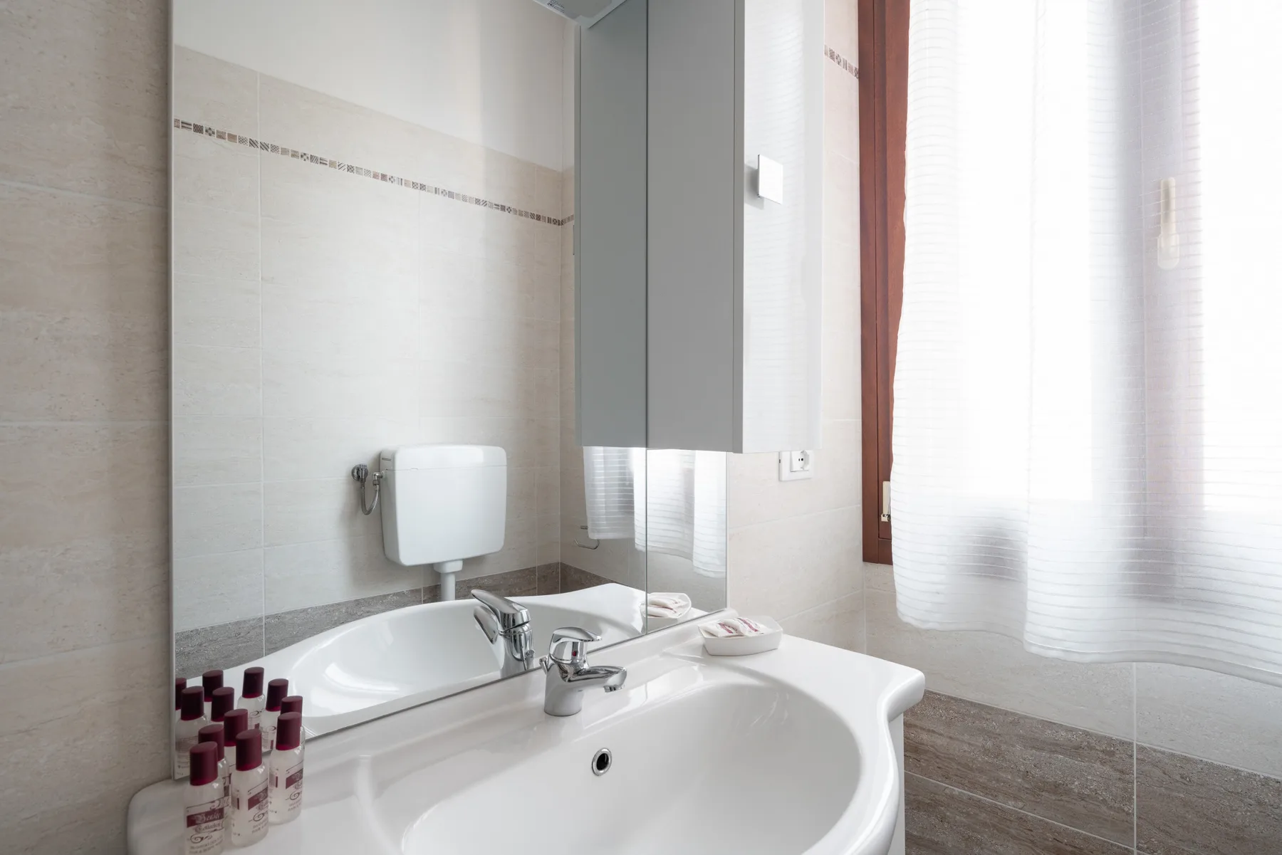 Un baño luminoso con lavabo blanco, espejo y ventana.
