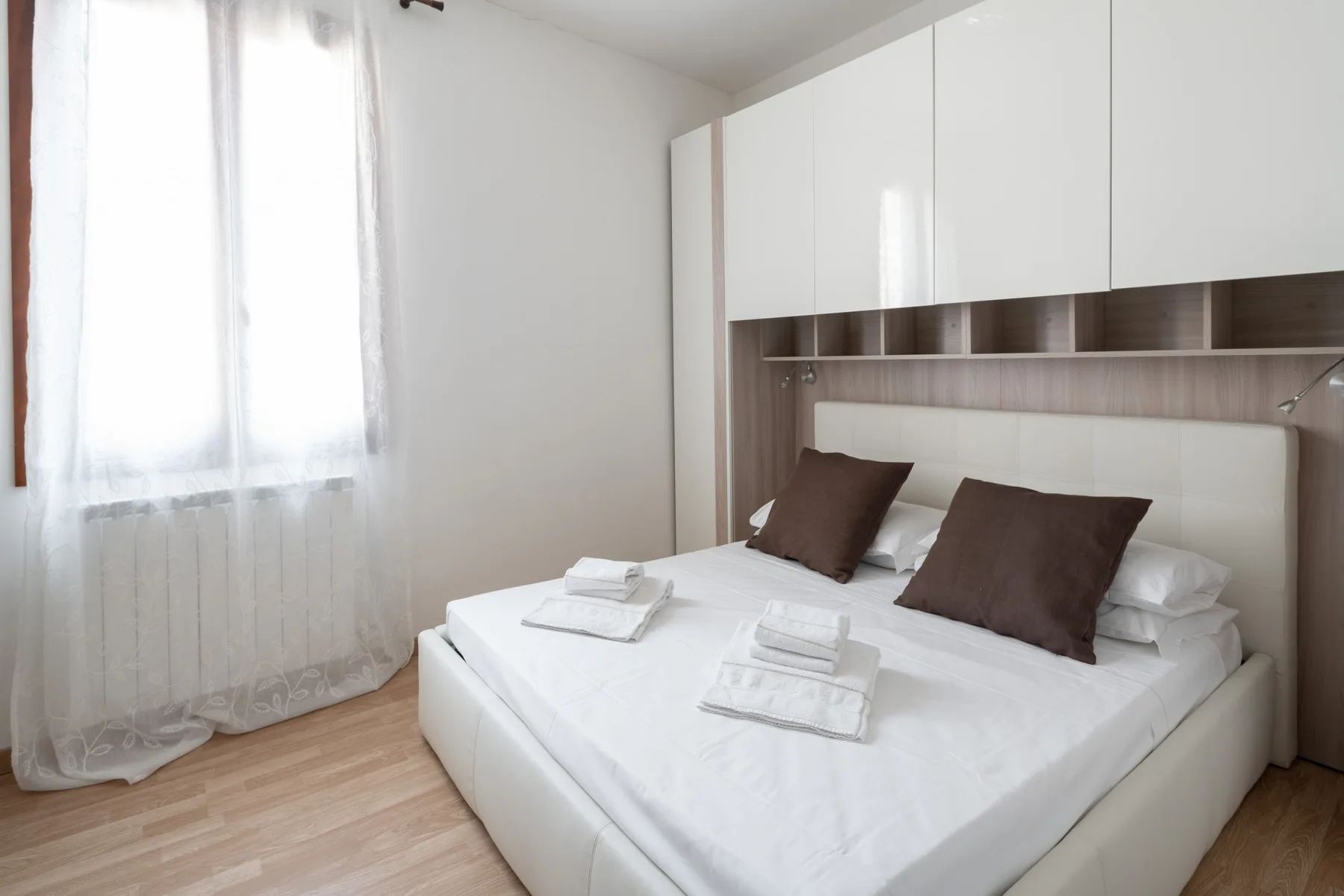 Un dormitorio luminoso con una cama tendida y armarios blancos.