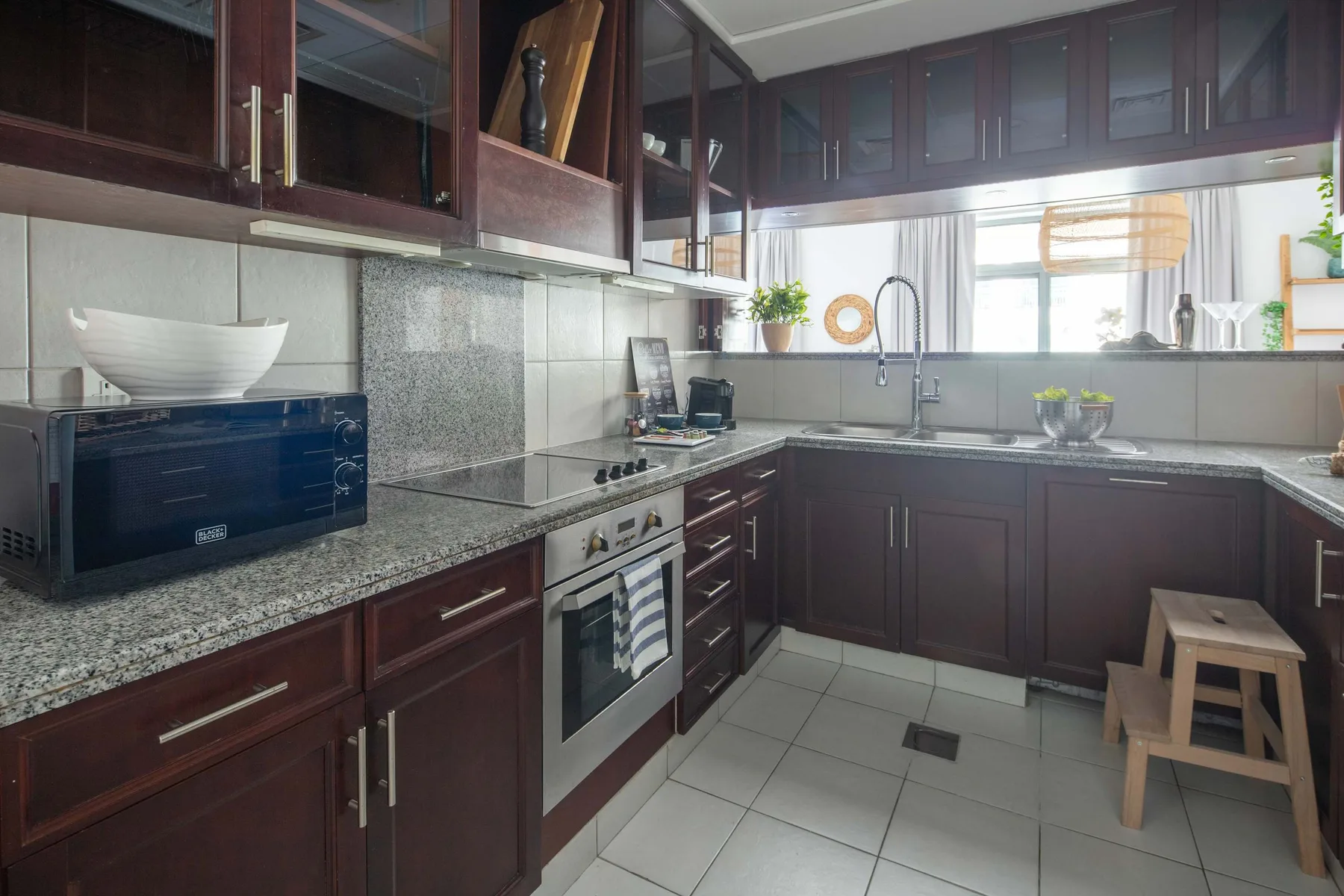 A kitchen with dark cabinetry, stone counters, and a sink beneath the window.