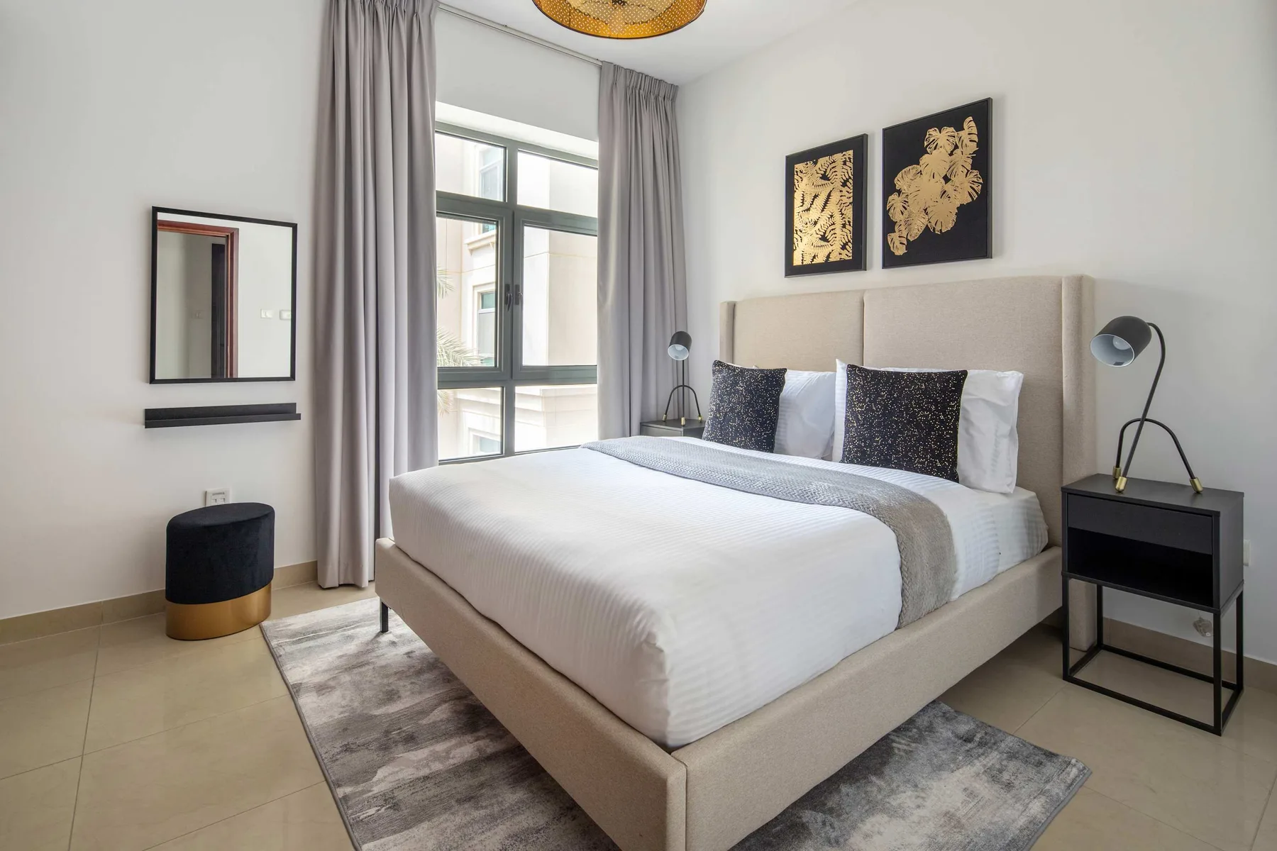 A bright bedroom with a neatly made bed and tall curtained window.