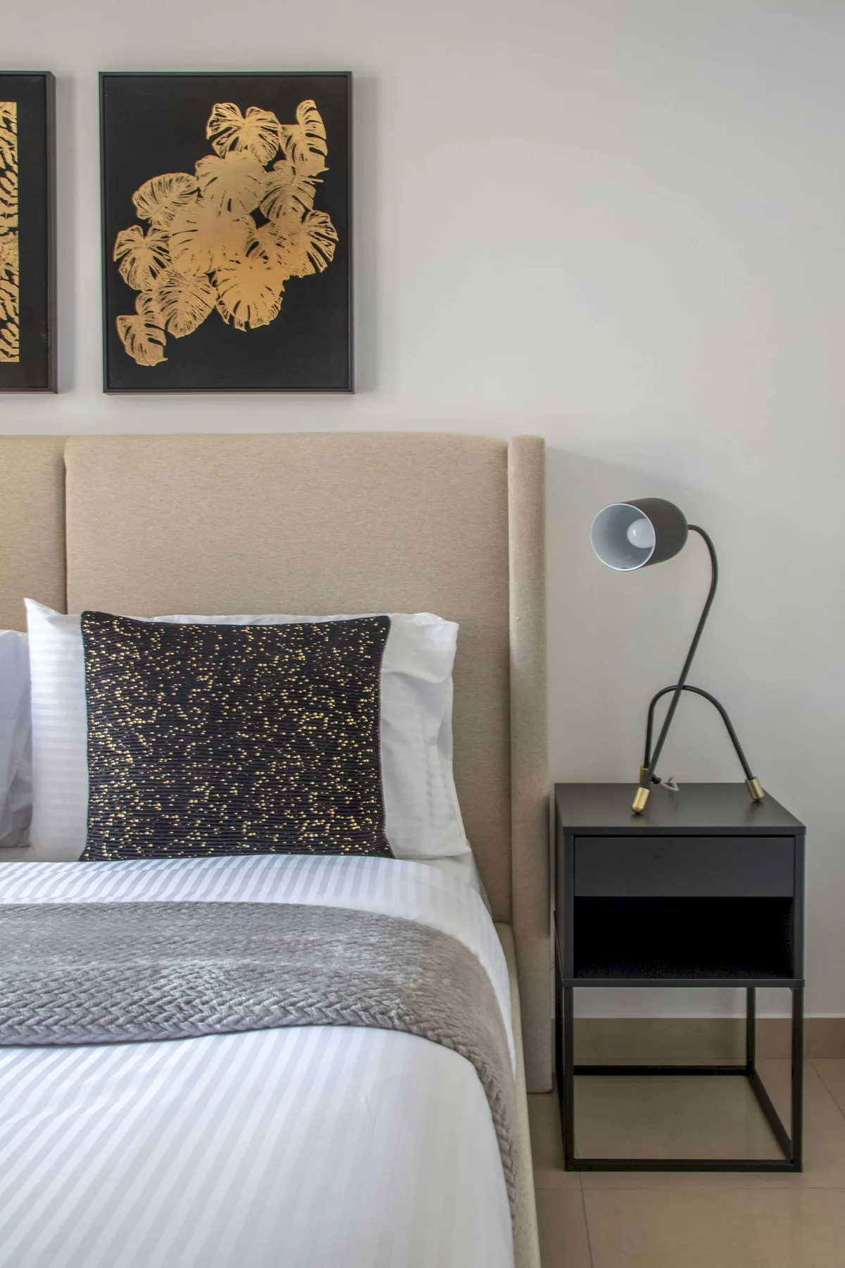 A bedroom with a neatly made bed, dark accent pillow, and bedside table.