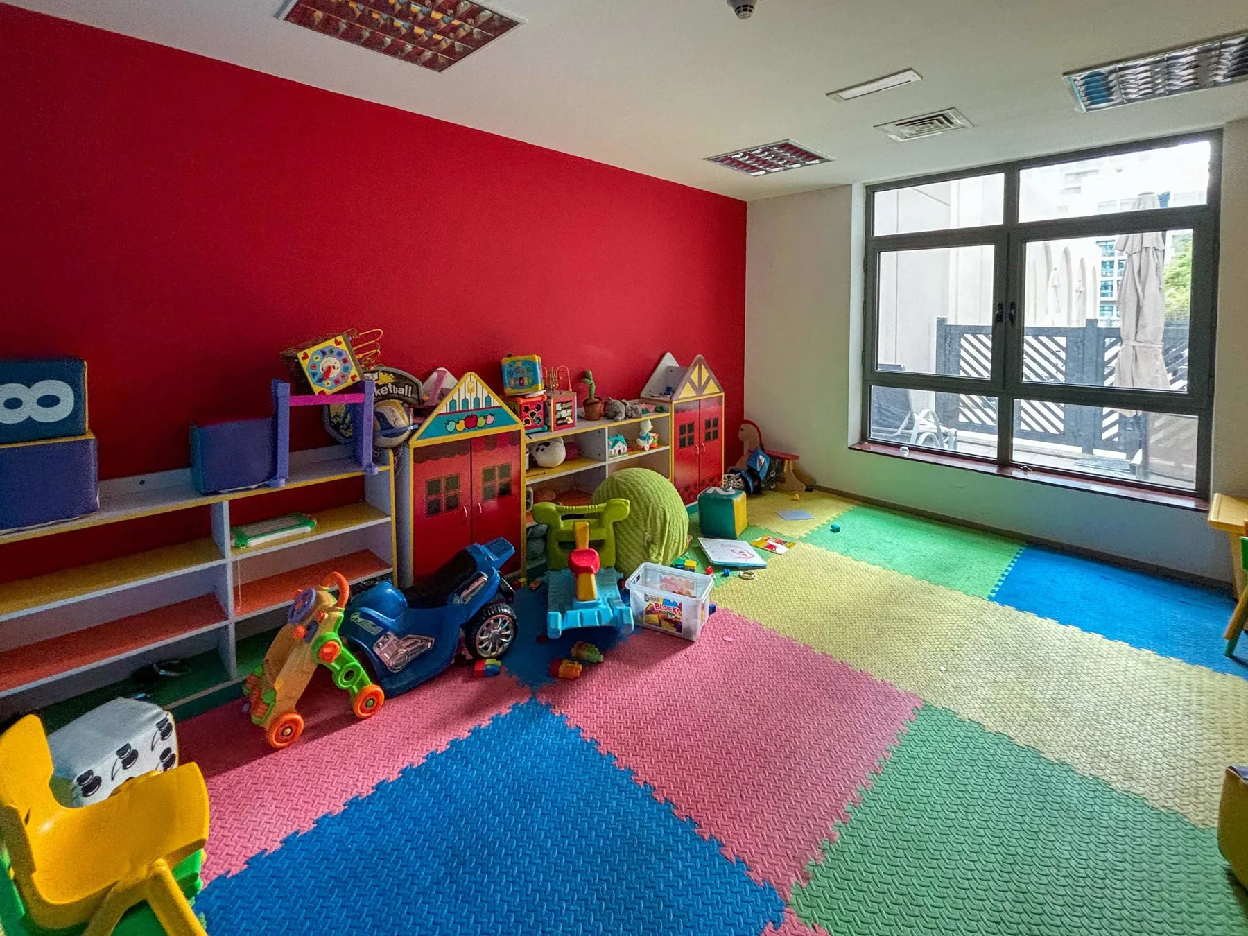 A colorful playroom with toys, low shelves, and bright interlocking floor mats.
