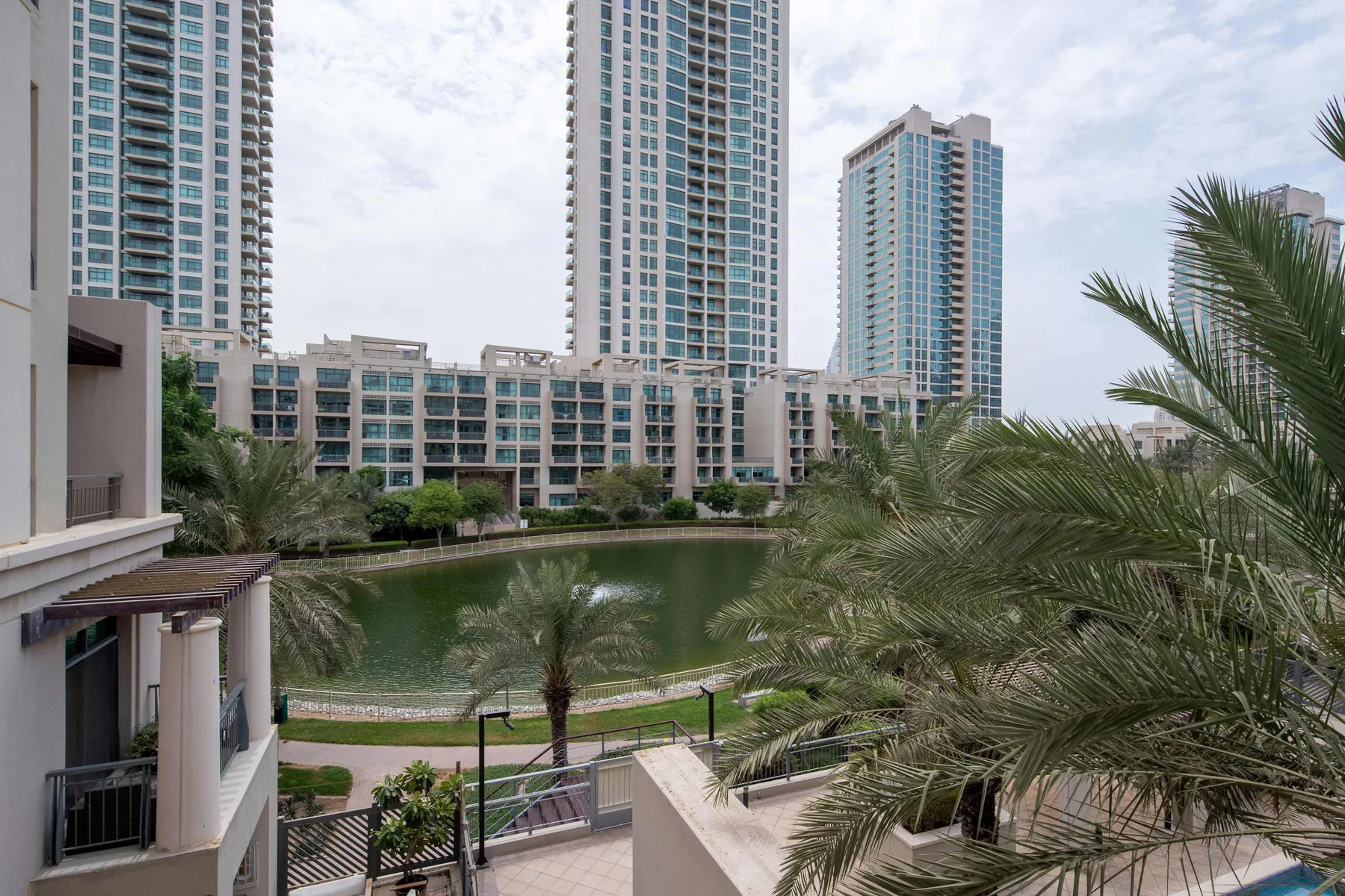 Residential towers overlook a landscaped pond lined with palm trees.