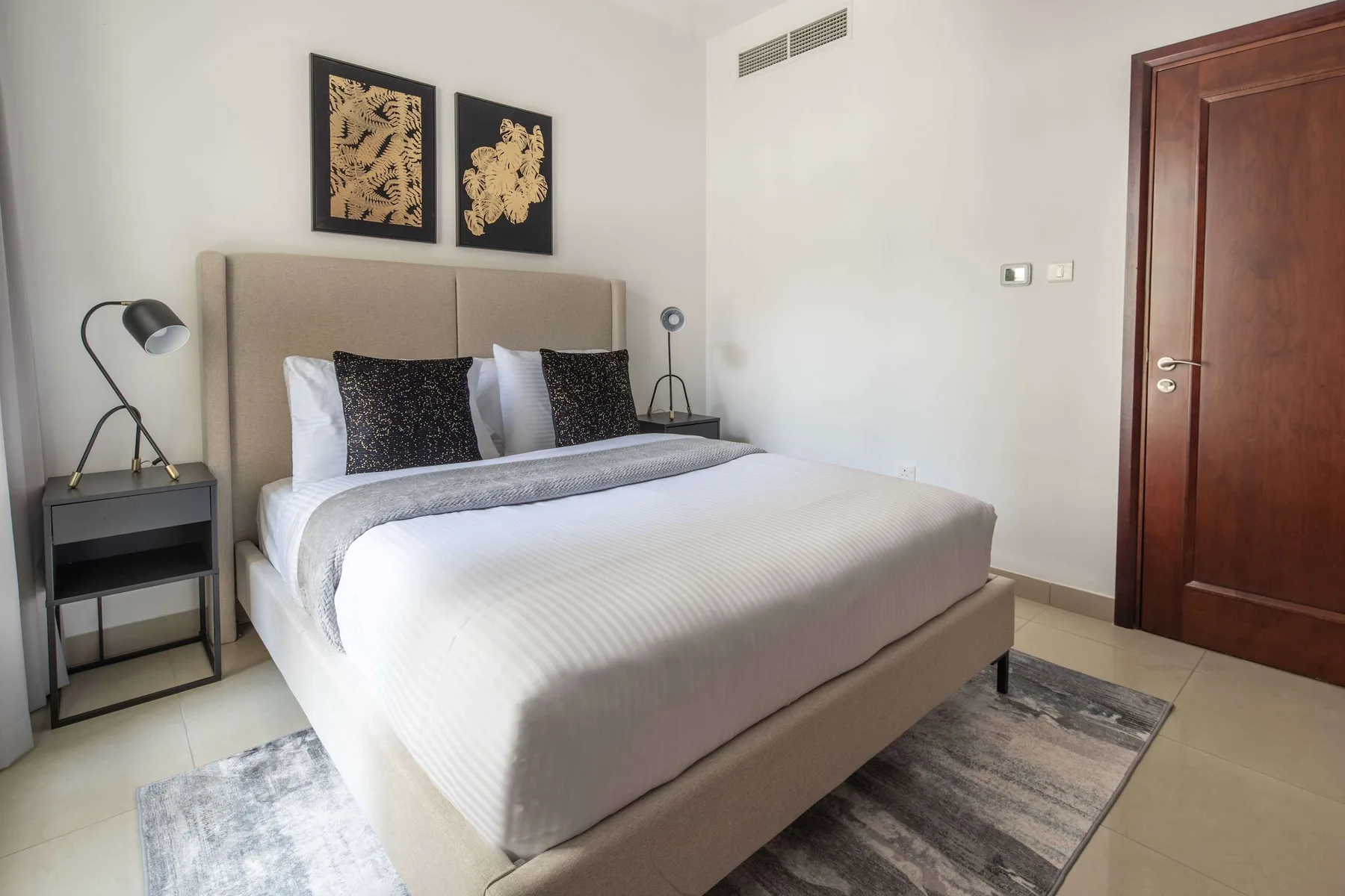 A bedroom with a neatly made bed and two framed artworks above the headboard.
