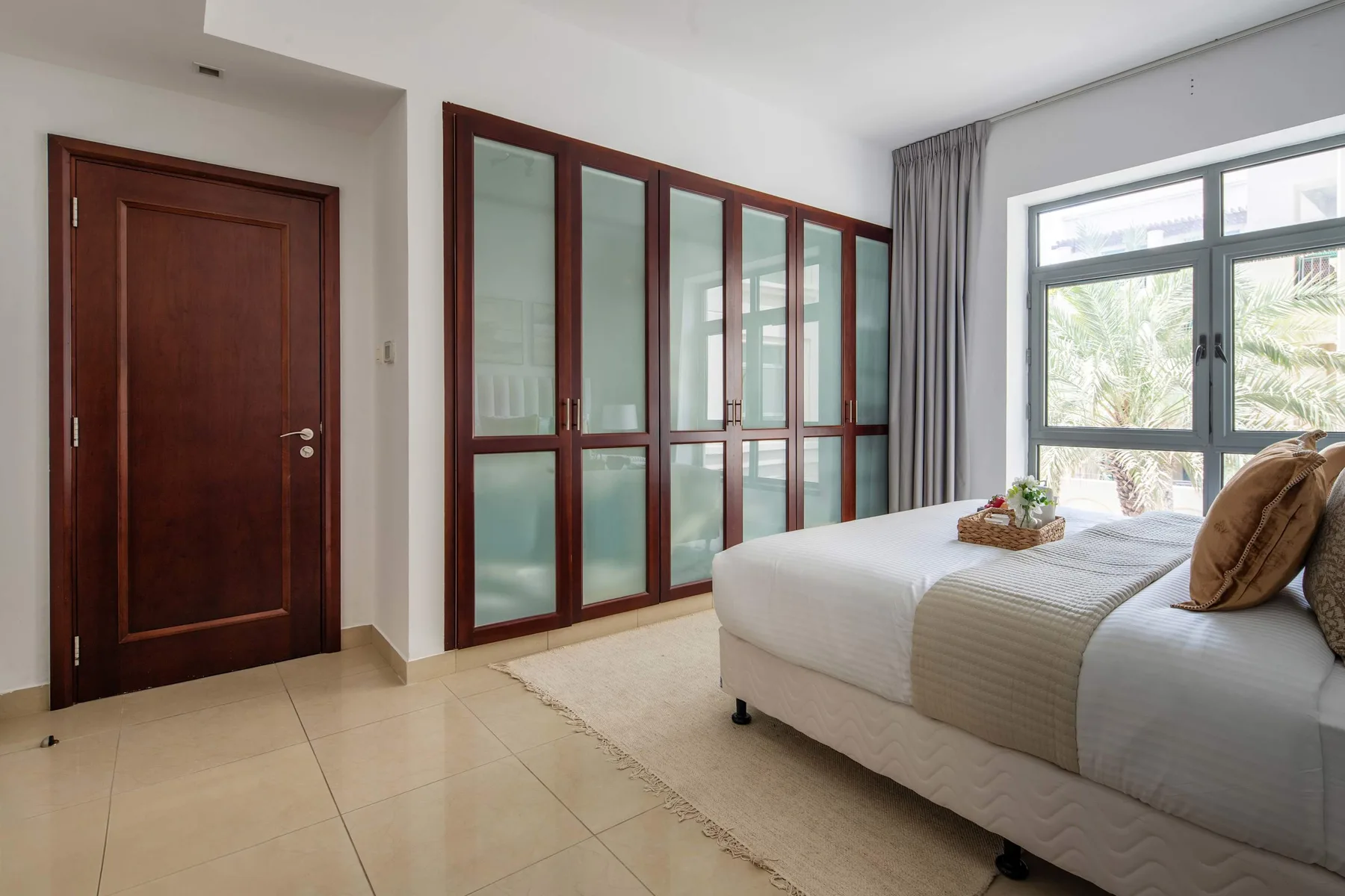A bright bedroom with a large bed, built-in cabinets, and a window.