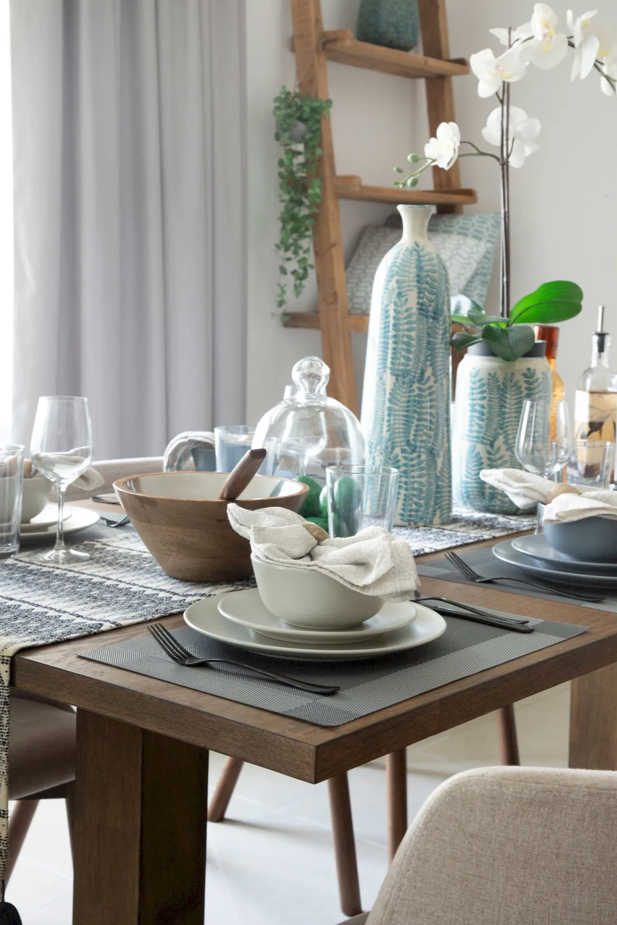 A dining table is set with plates, bowls, glassware, and tall vases.