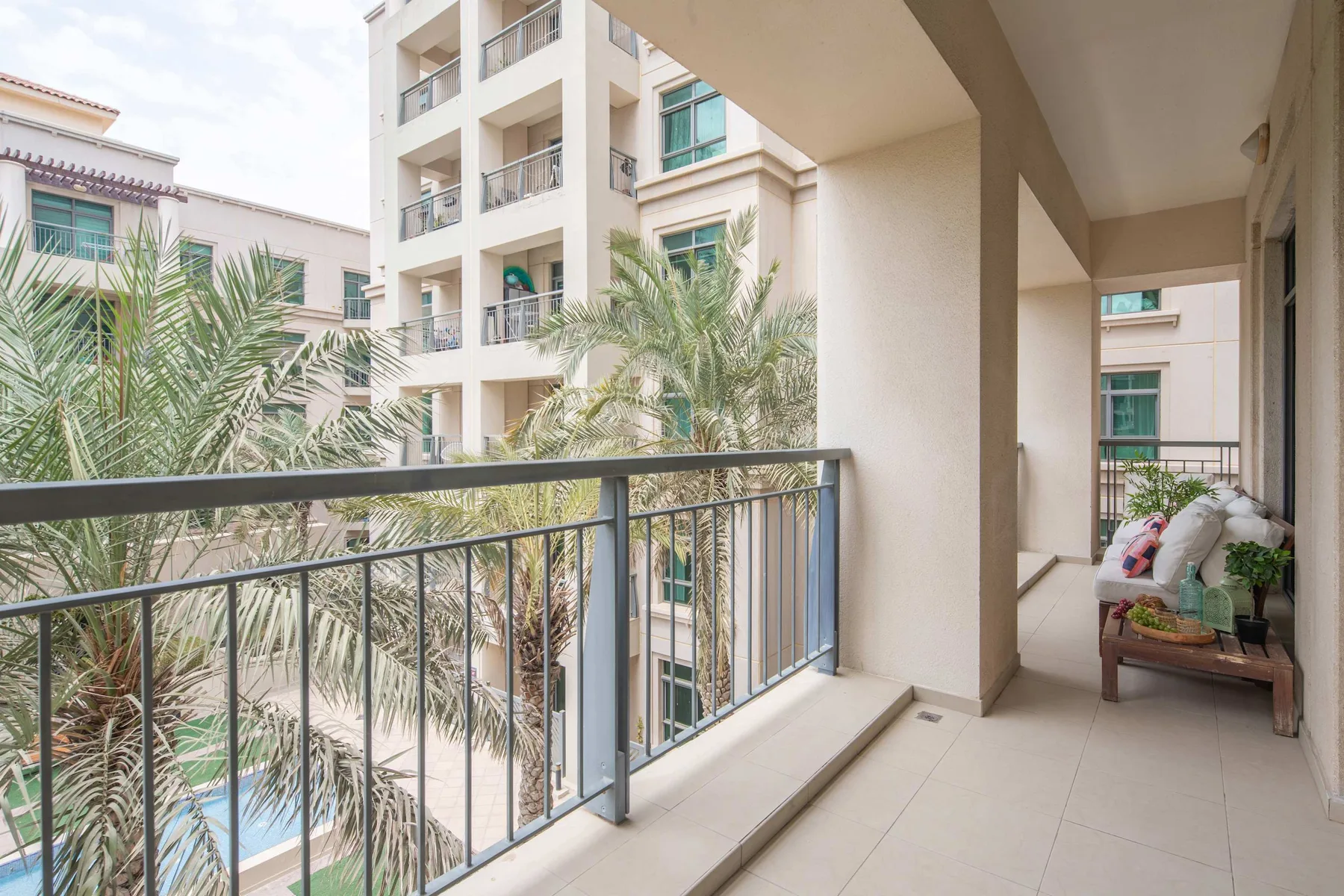 A balcony overlooks palm trees and neighboring apartment buildings, with seating at the far end.