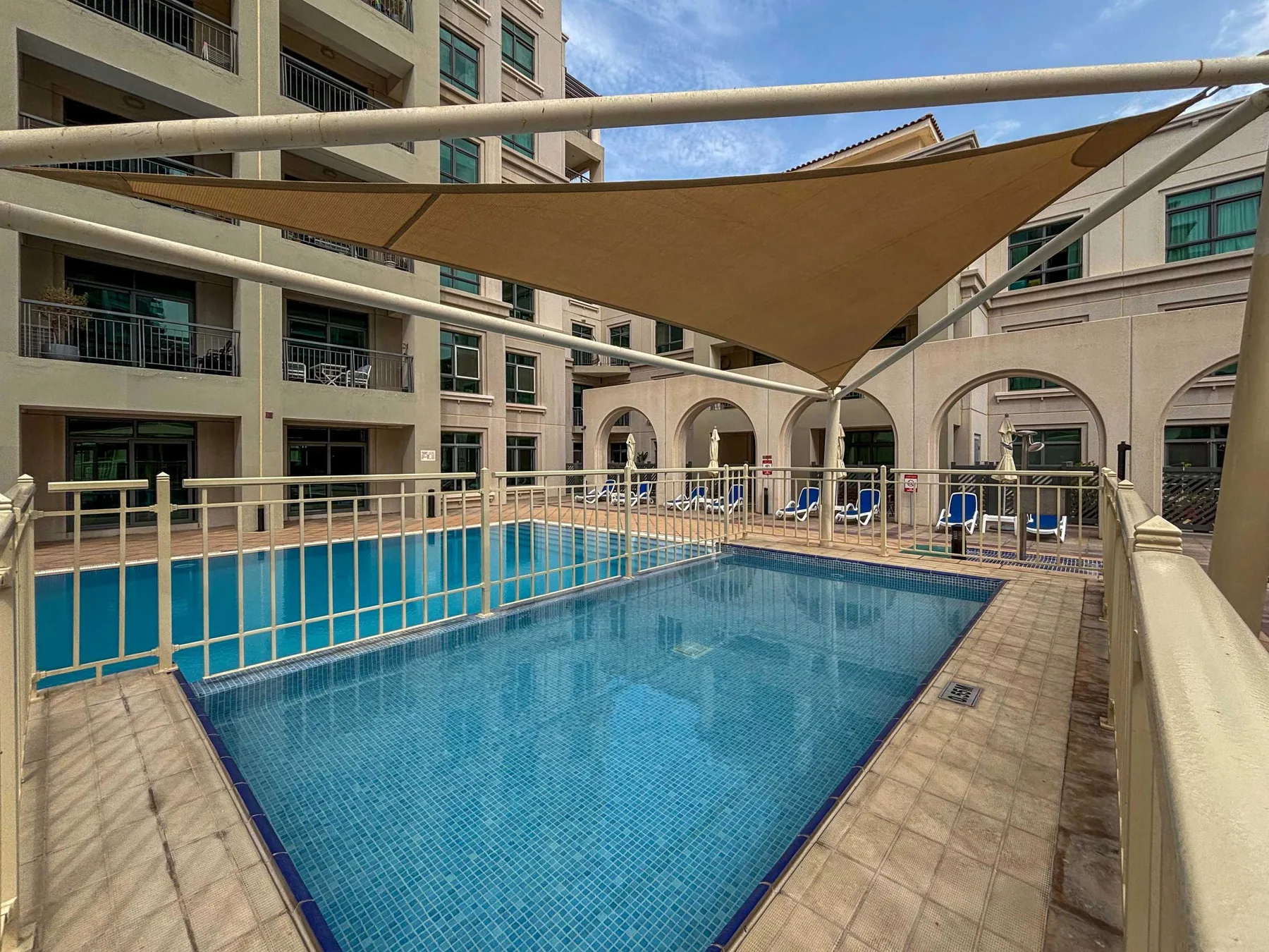An outdoor swimming pool sits beneath a shade canopy in a courtyard.