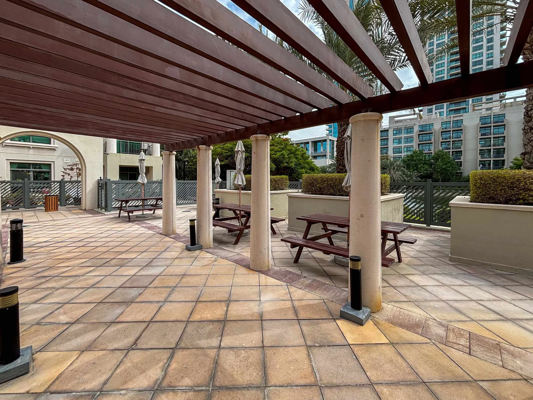 A paved outdoor patio with picnic tables beneath a wooden pergola.
