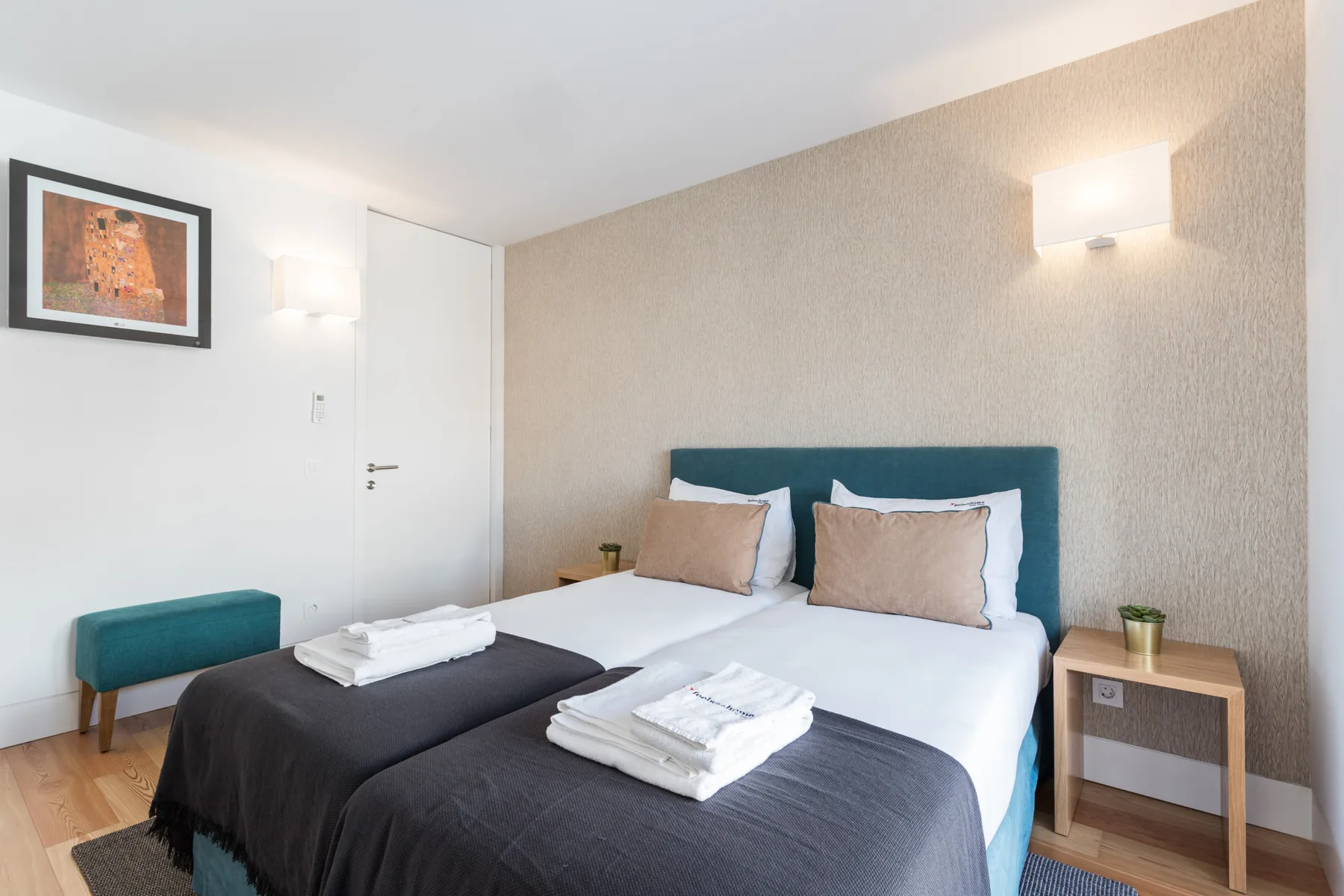 Un dormitorio con una cama doble, toallas dobladas y un cabecero tapizado en verde azulado.