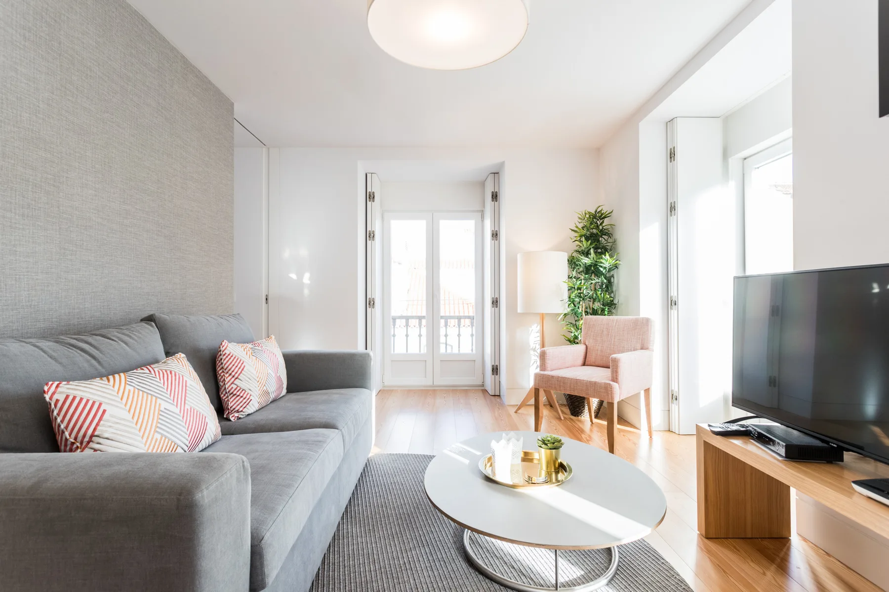 Una sala de estar luminosa con un sofá gris y una mesa de centro redonda.