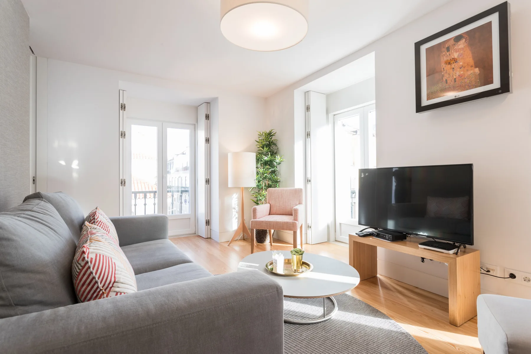 Una sala de estar luminosa con asientos, un televisor y puertas que dan a un balcón.