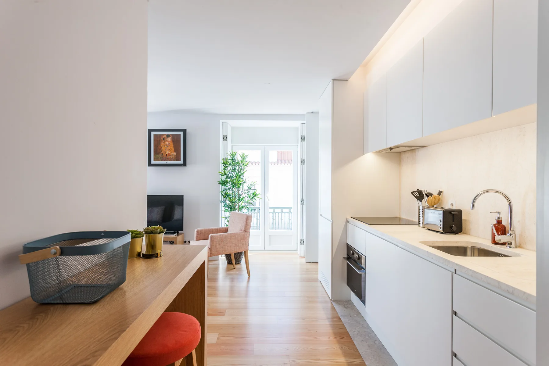 Una cocina y zona de comedor luminosa, con armarios blancos y una mesa junto a la ventana.