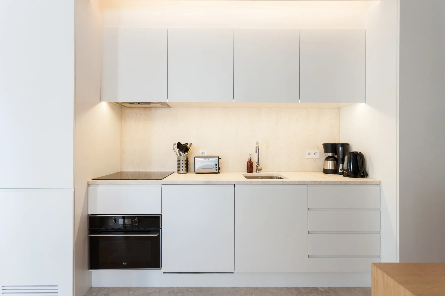 Una cocina moderna y luminosa con armarios blancos y pequeños electrodomésticos.
