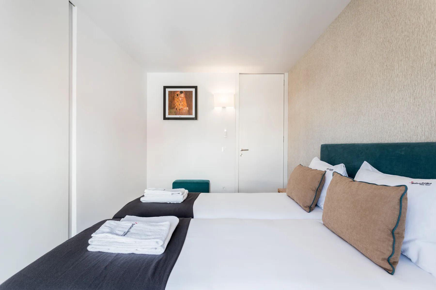 Un dormitorio luminoso con dos camas, toallas dobladas y un cuadro enmarcado.