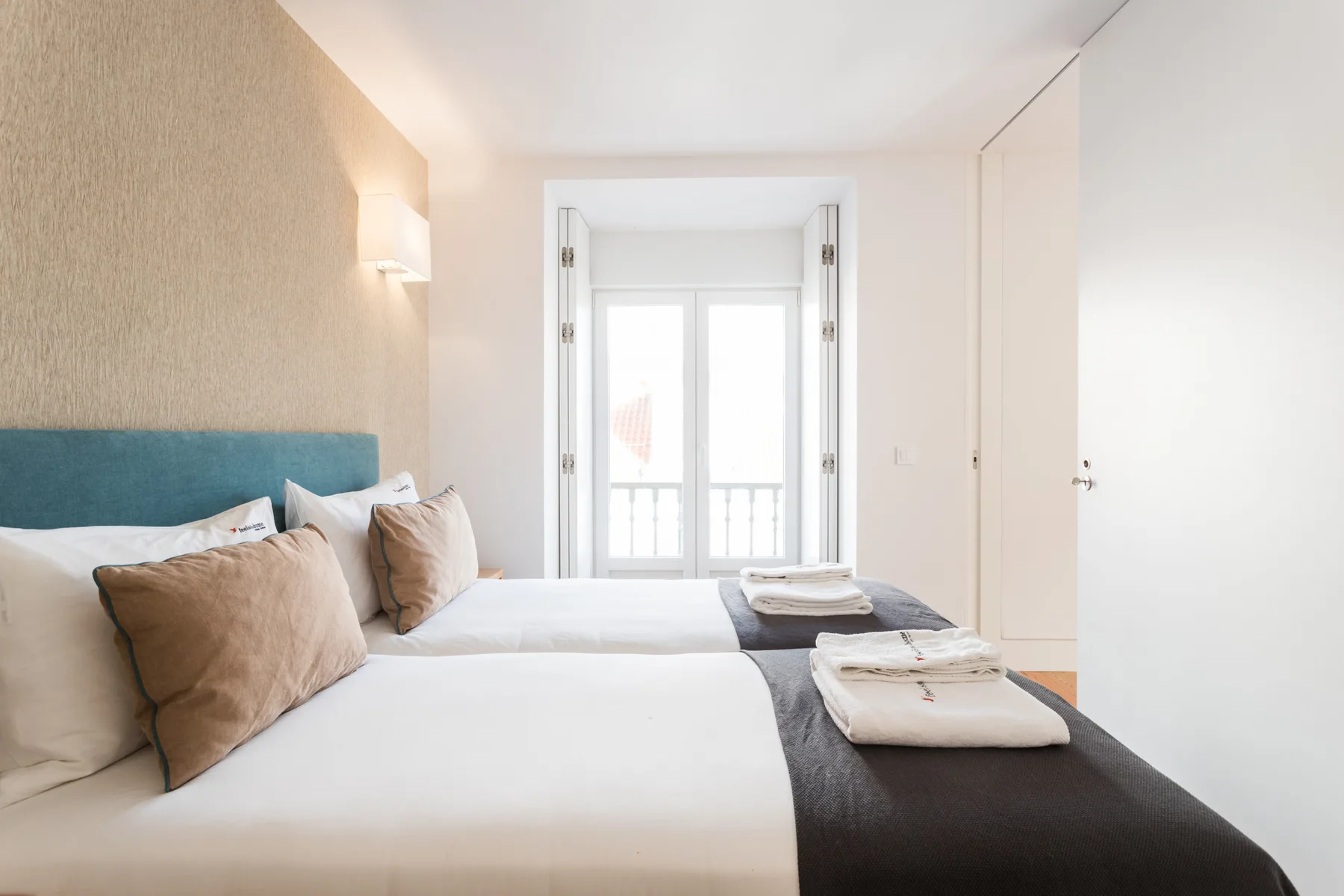 Un dormitorio luminoso con una cama, toallas dobladas y una ventana.