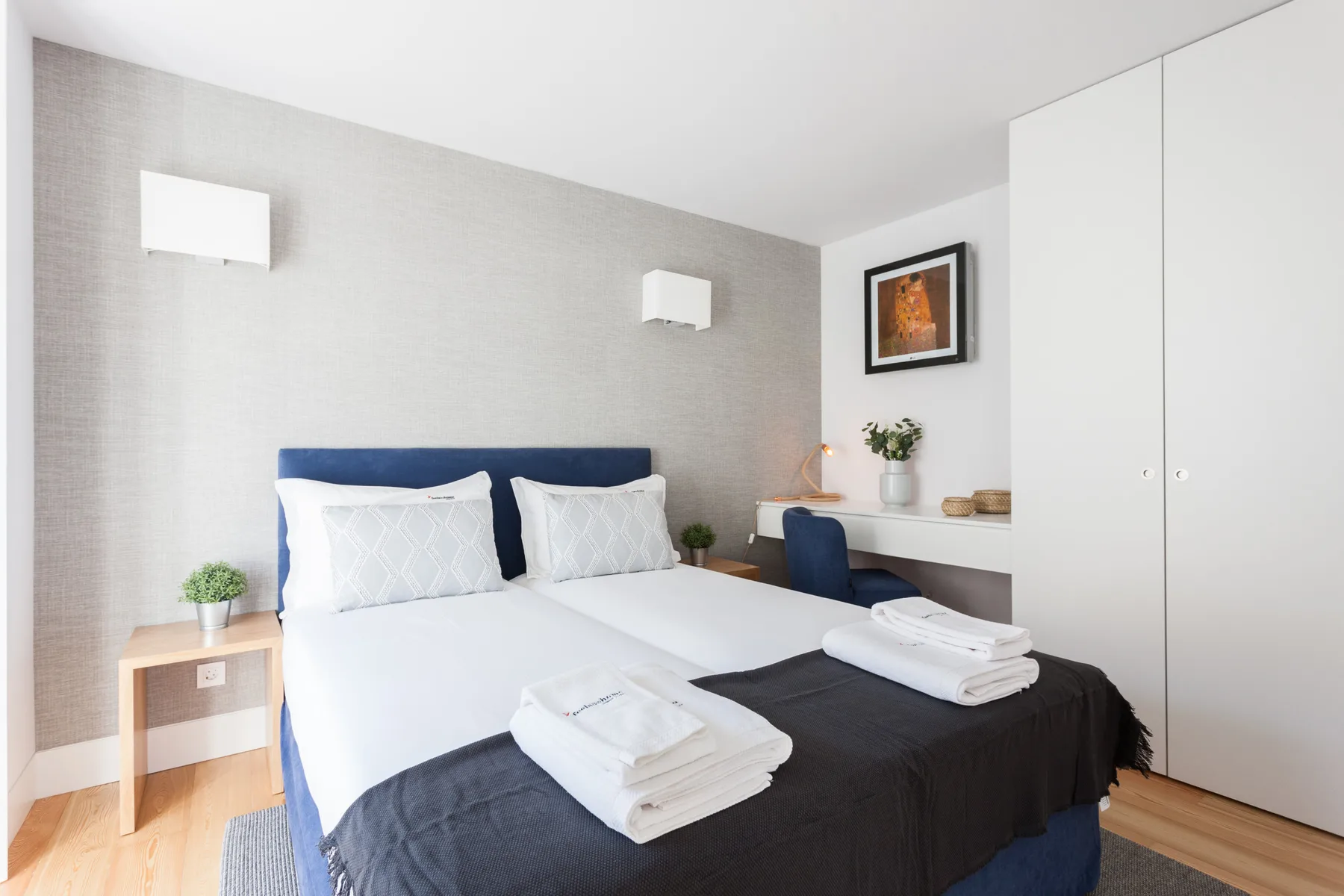 Un dormitorio con una cama vestida con sábanas blancas y ropa de cama oscura.