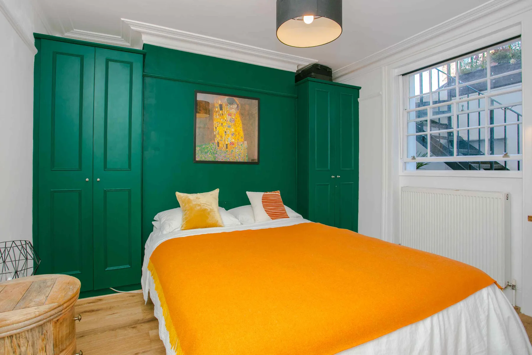 A bedroom with a bed covered by a bright orange blanket and green built-in cabinets.