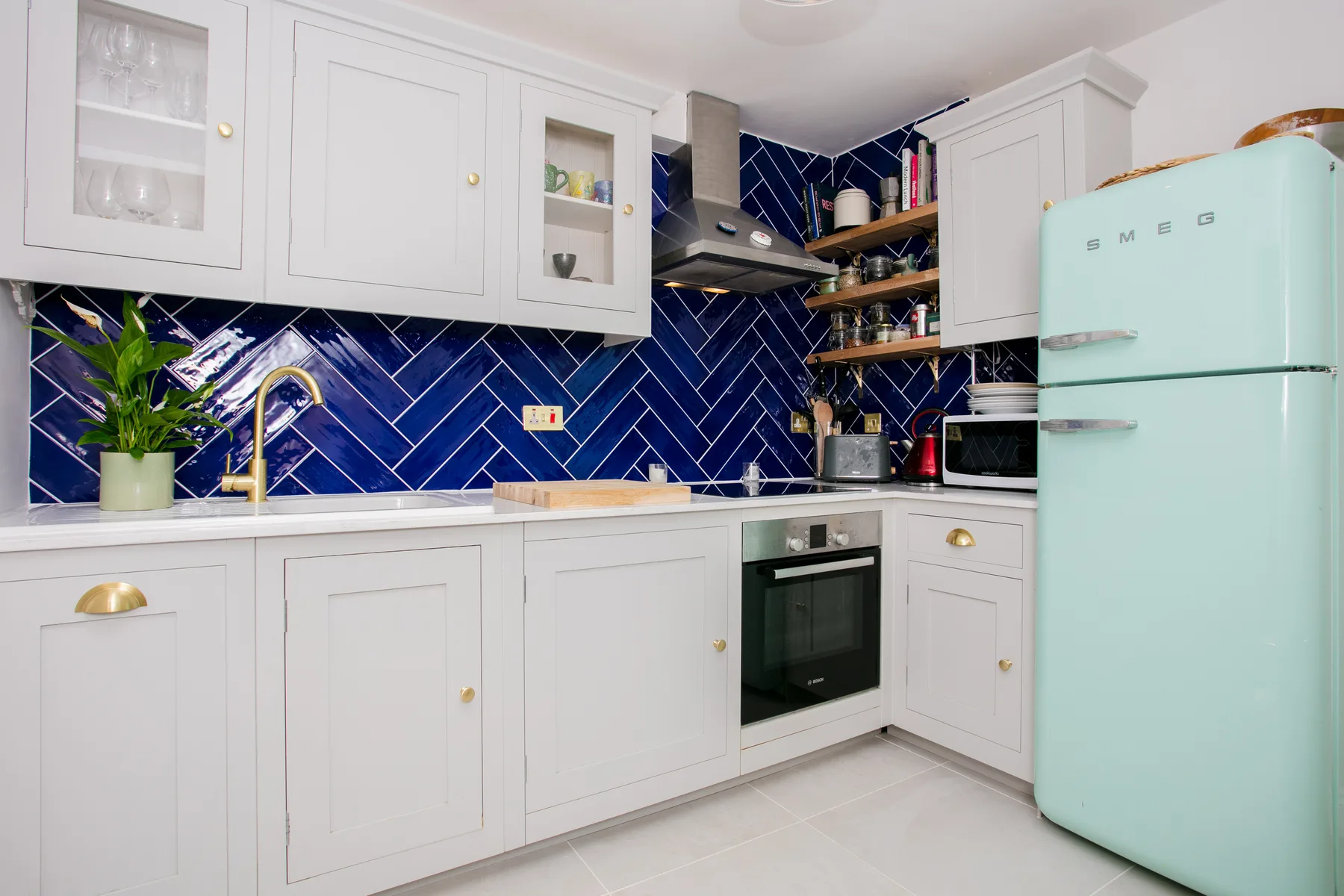 A bright kitchen with white cabinets, dark blue backsplash, and a mint refrigerator.