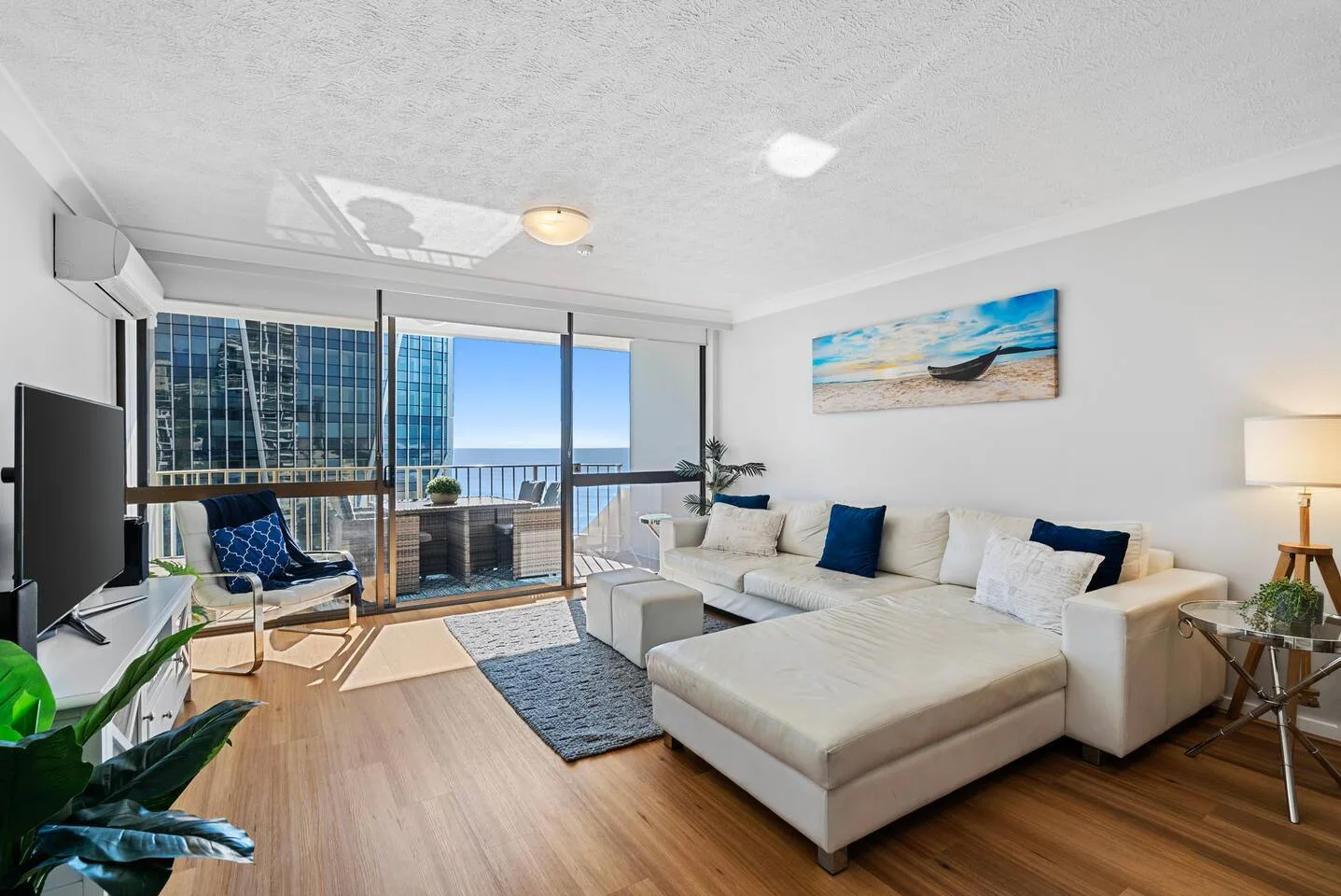 A bright living room with a white sectional sofa facing sliding glass doors and a balcony.