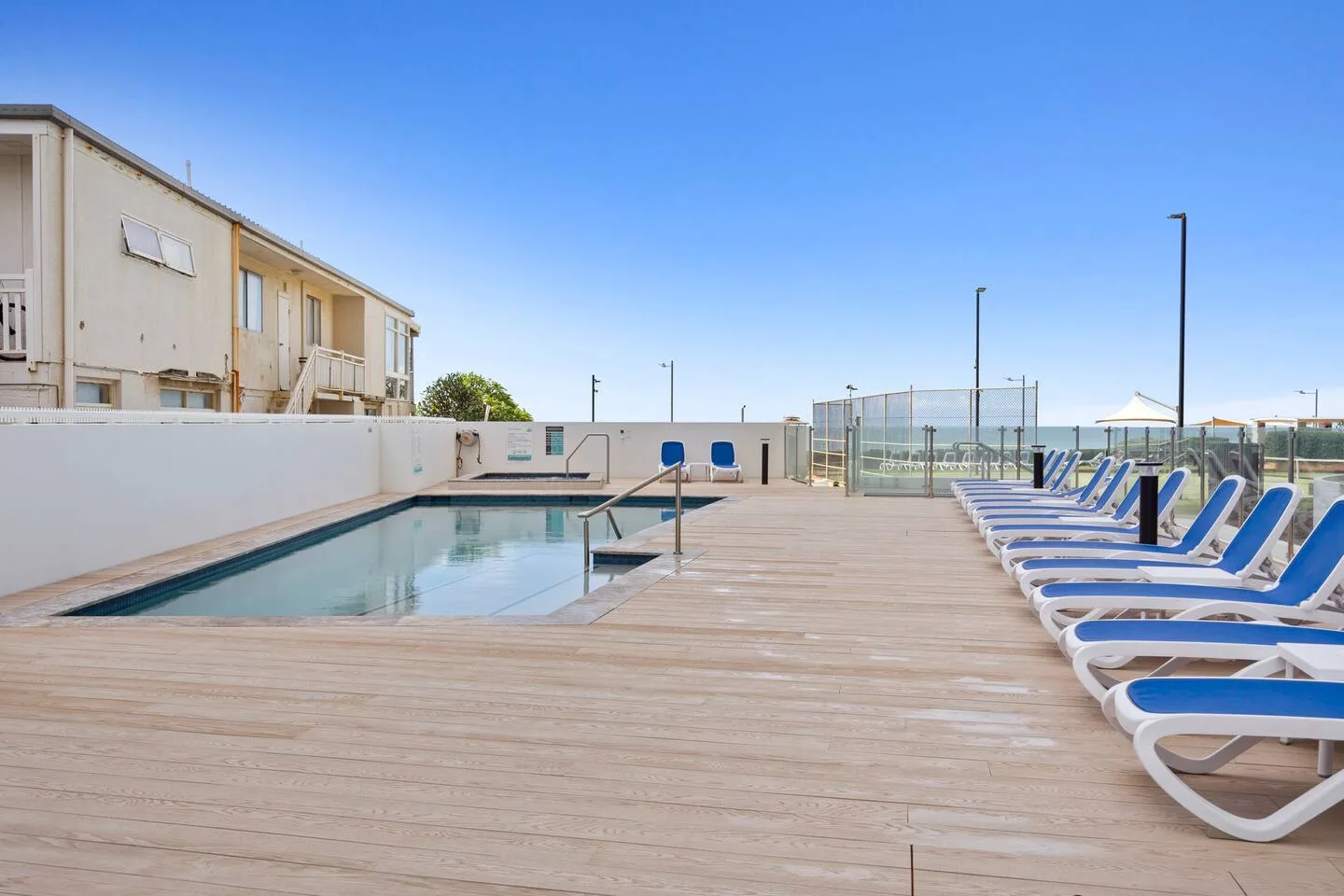 An outdoor swimming pool beside a wooden deck lined with sun loungers.