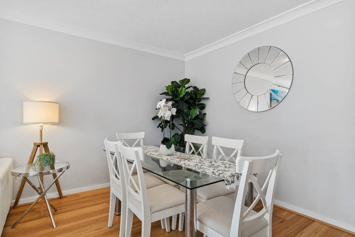 A dining area with a glass table, white seating, and a potted plant.